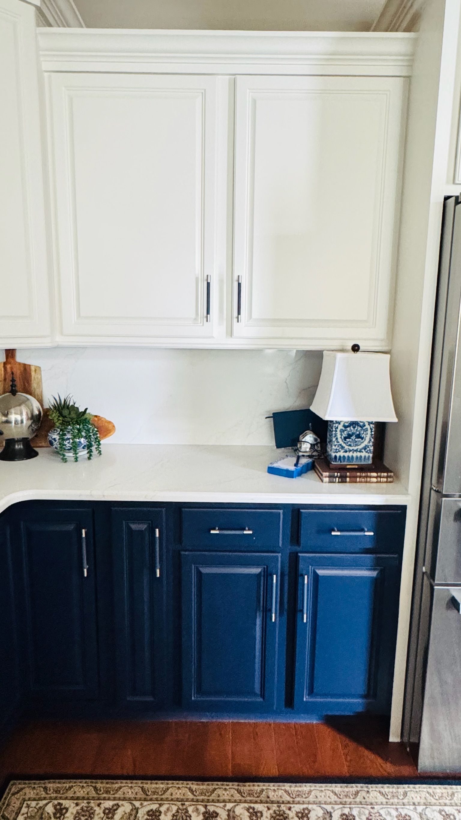 Kitchen cabinets: white upper cabinets, navy blue lower cabinets, white countertop, lamp and decor.