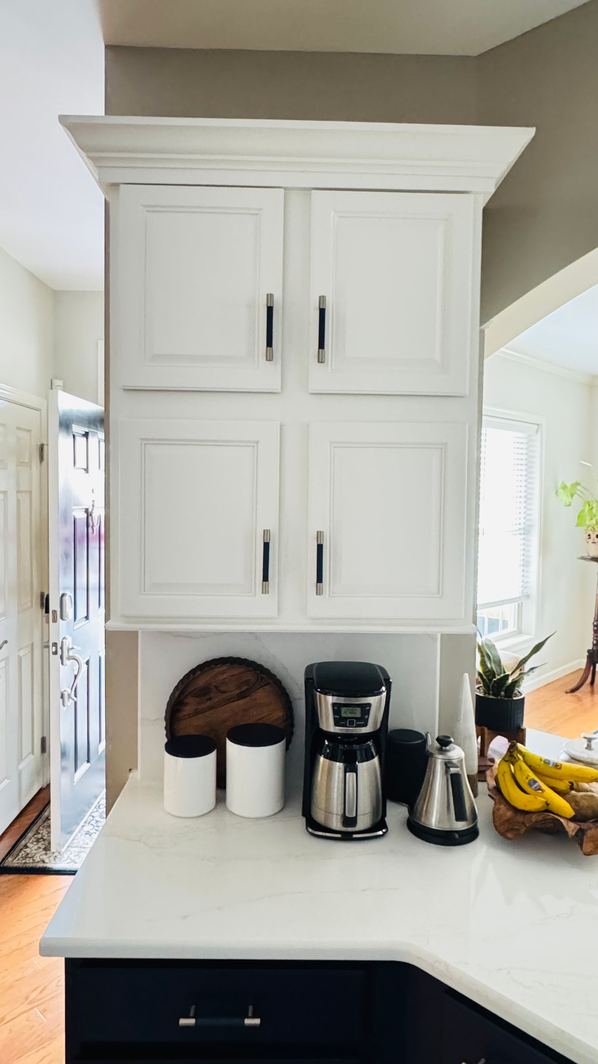 White kitchen cabinets above a countertop with coffee maker, accessories, and bananas.