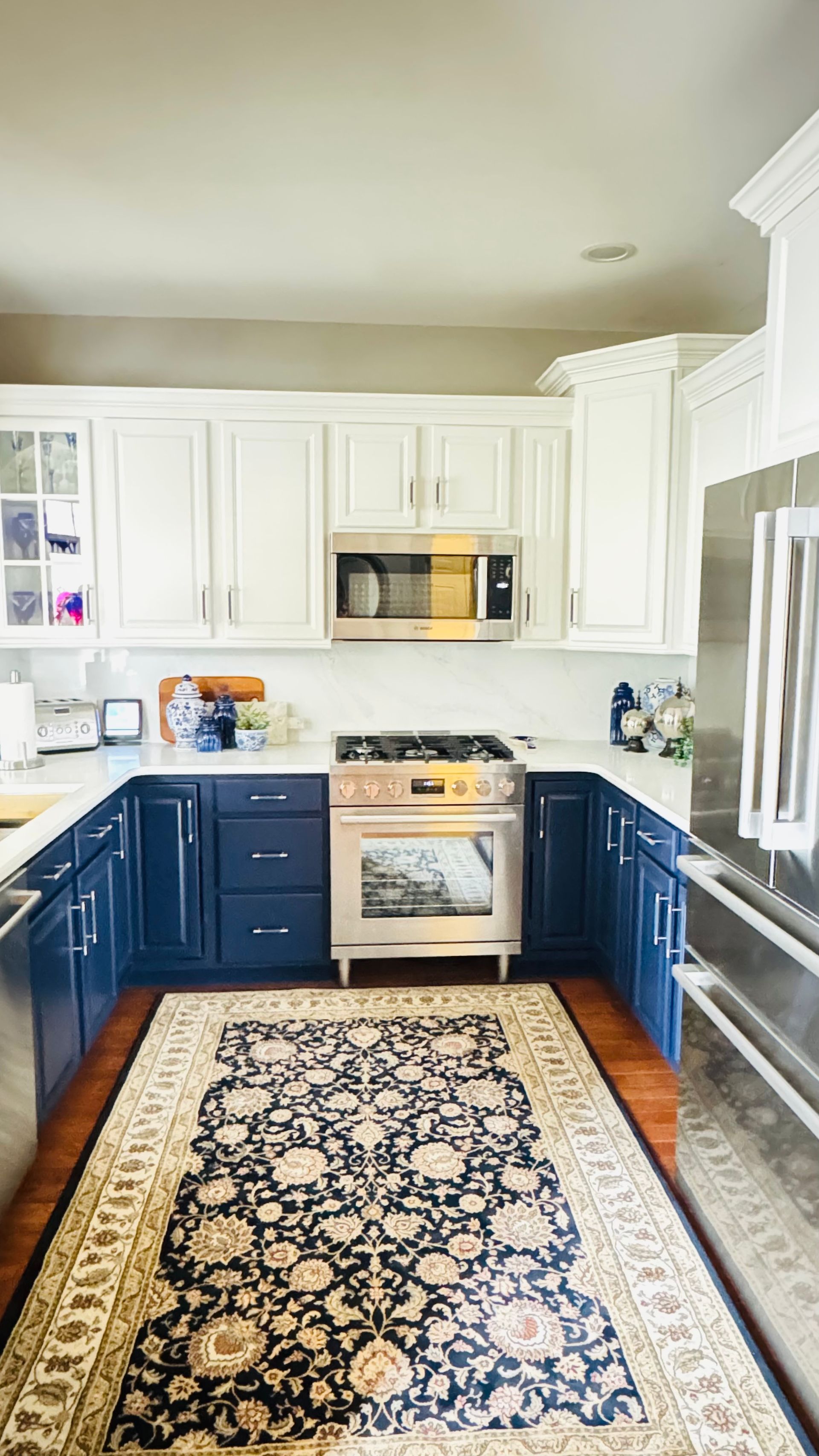 U-shaped kitchen with blue lower cabinets, white uppers, stainless appliances, and a patterned rug.