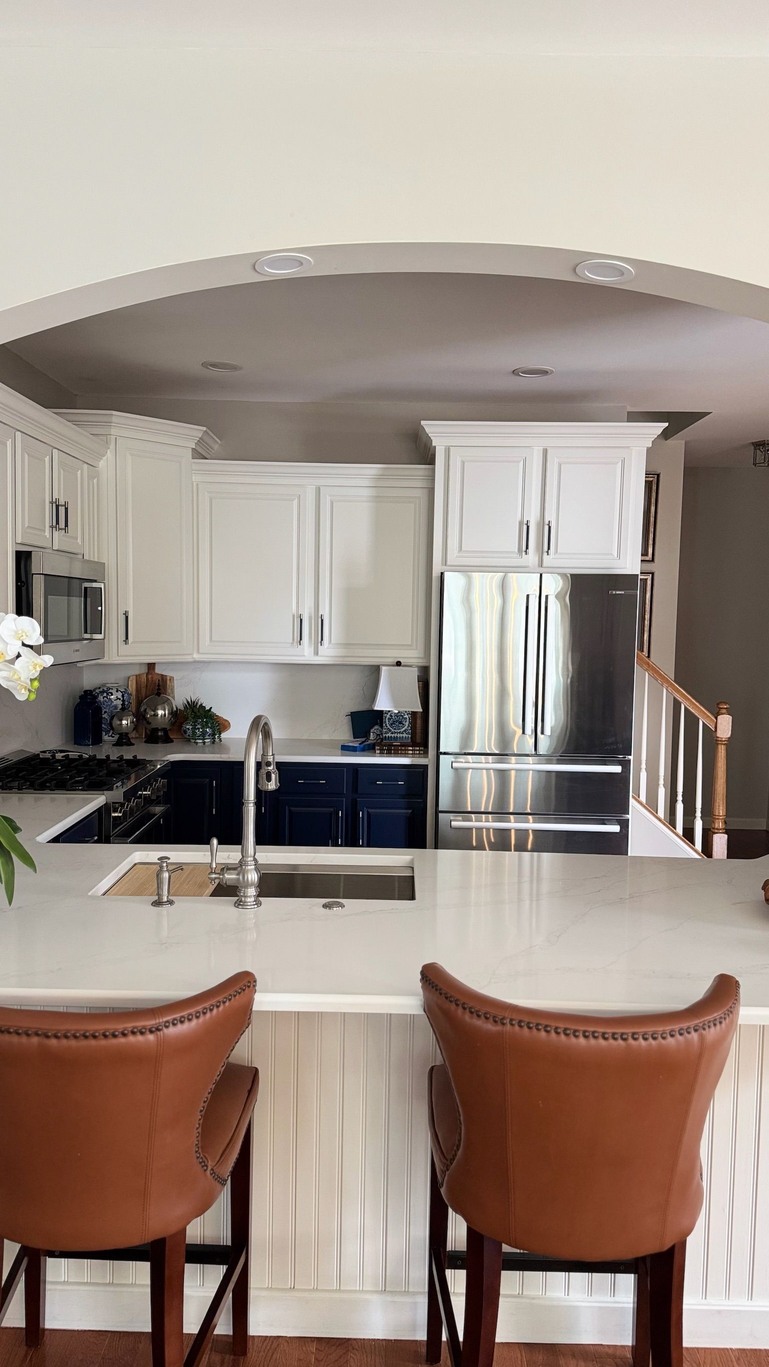 Kitchen with white cabinets, blue island, stainless steel appliances, leather bar stools.