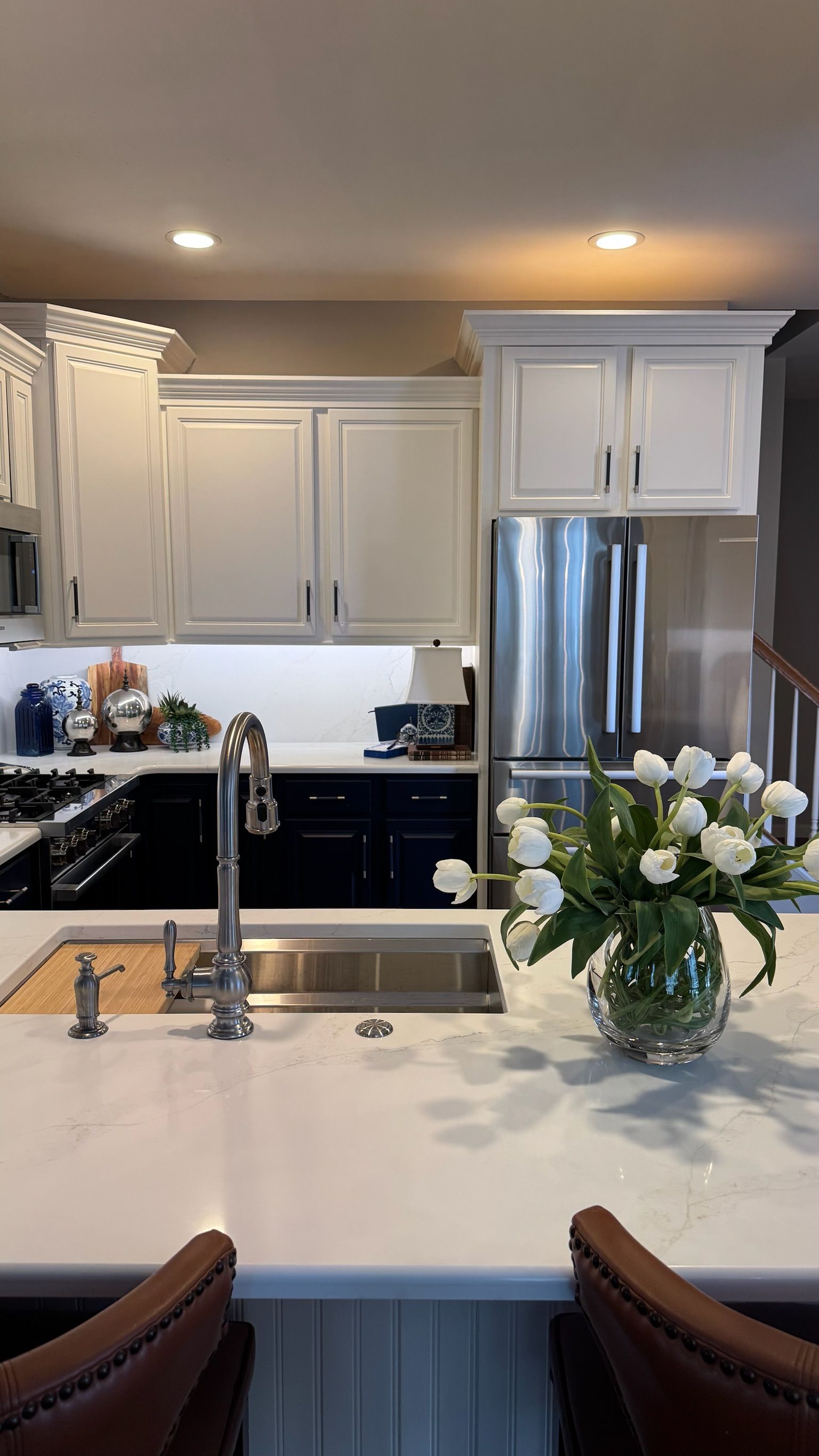 Kitchen with white cabinets, stainless steel appliances, white countertops, and a vase of white tulips.