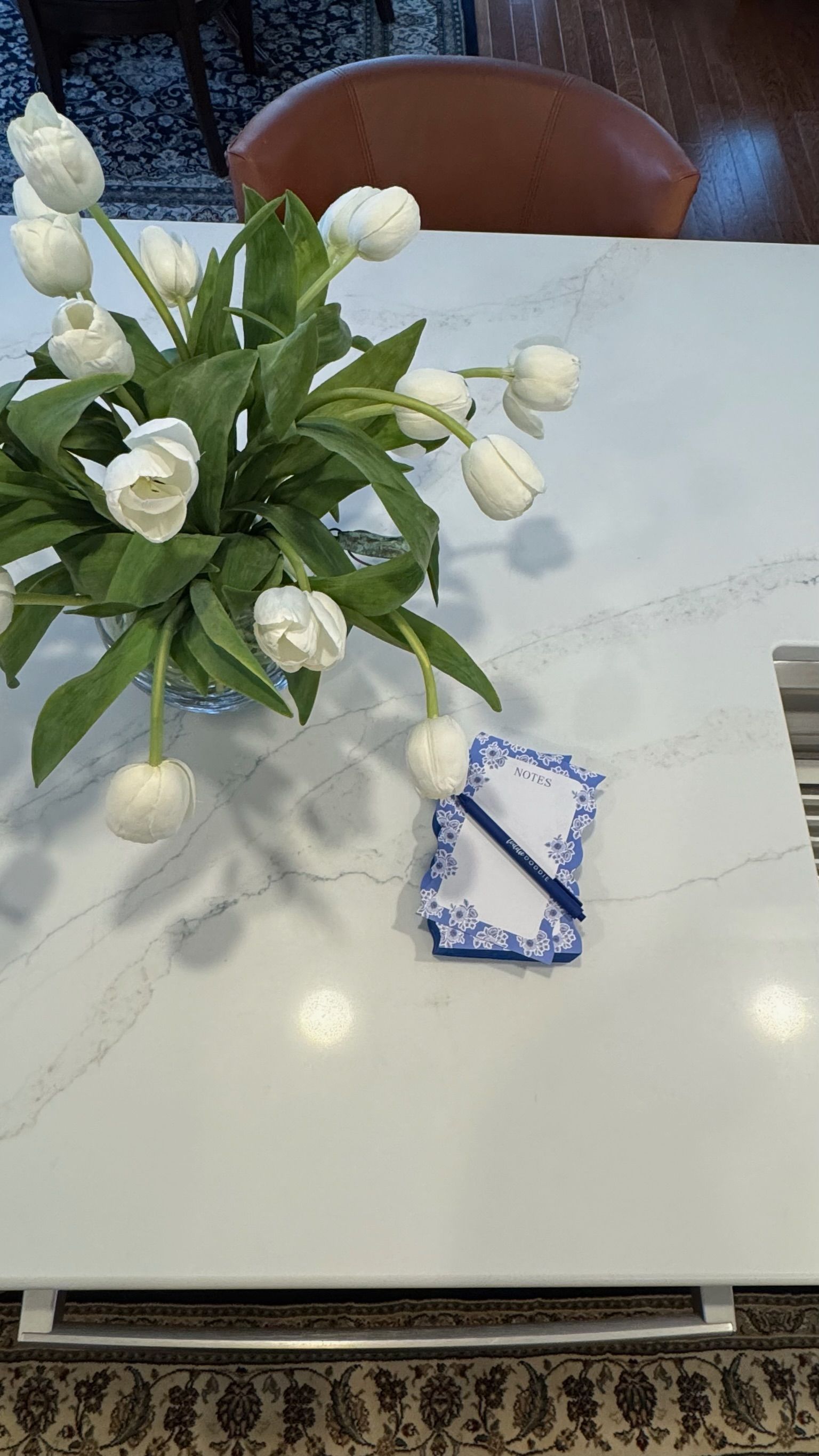 White tulips in vase beside notepad and pen on white countertop.