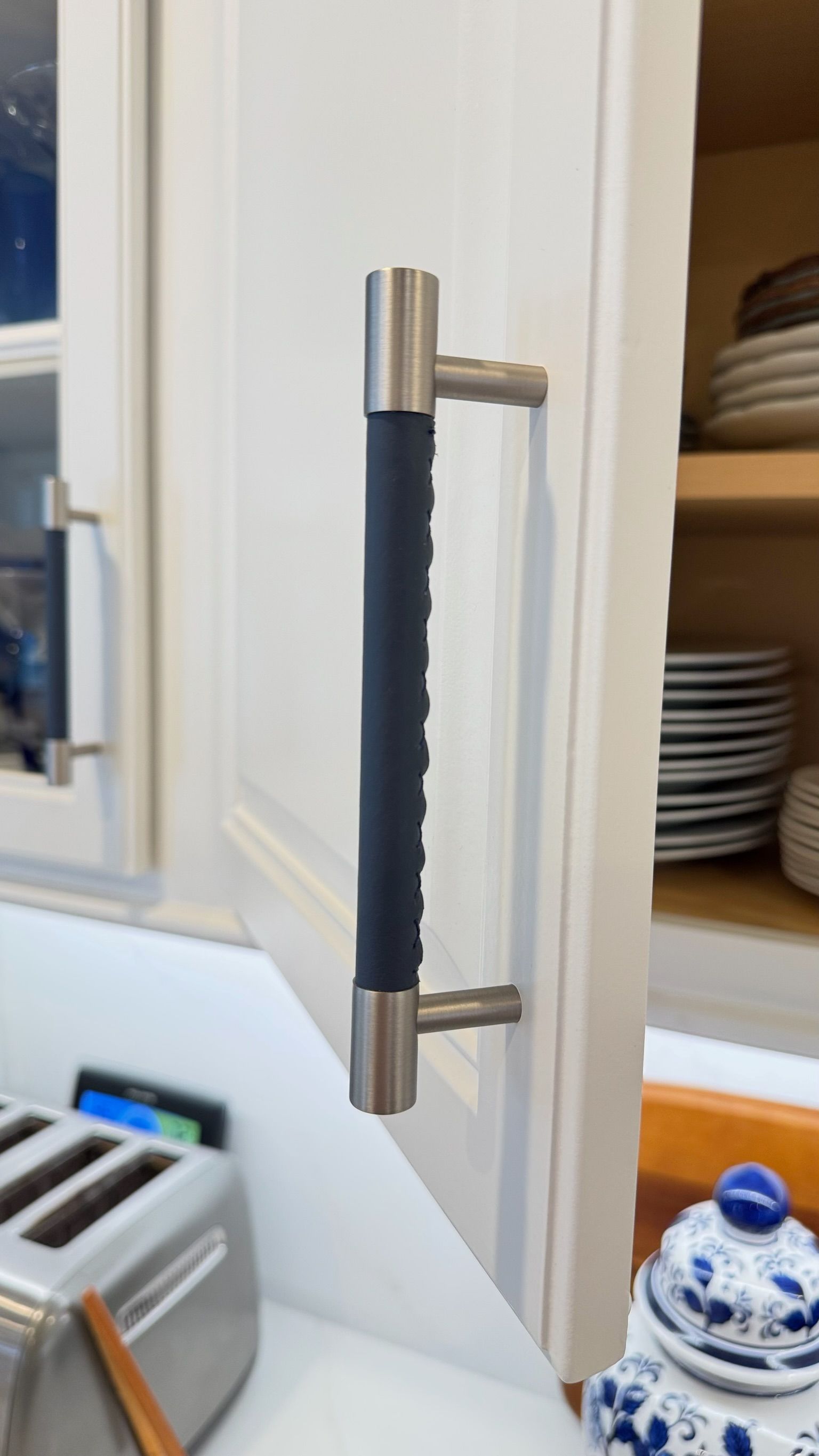 Cabinet door with stainless steel pull handle, black rubber grip. White cabinet with beige interior shelves.