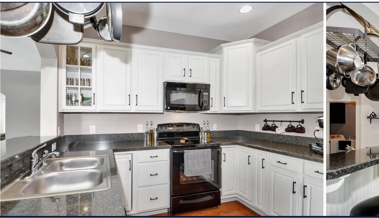 White kitchen with black countertops, stove, and cabinets. Stainless steel sink and hanging cookware.