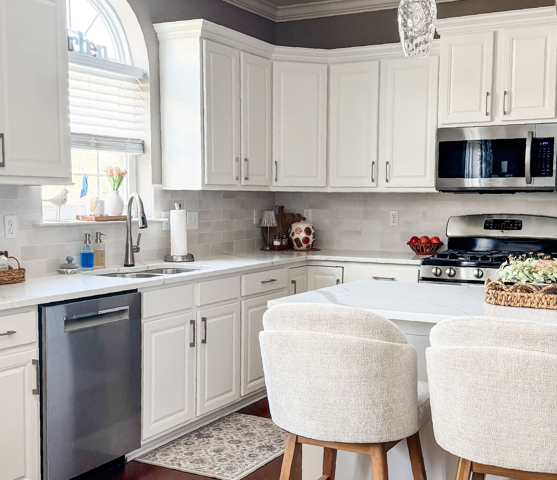 White kitchen with cabinets, stainless steel appliances, and two upholstered bar stools at an island.