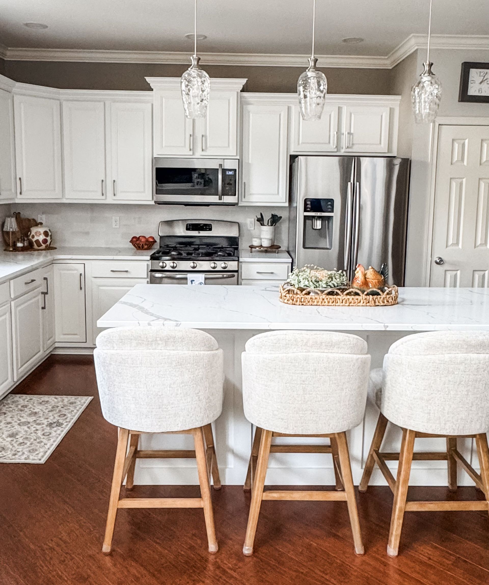 Bright kitchen with white cabinets, stainless steel appliances, and a marble island with three fluffy stools.