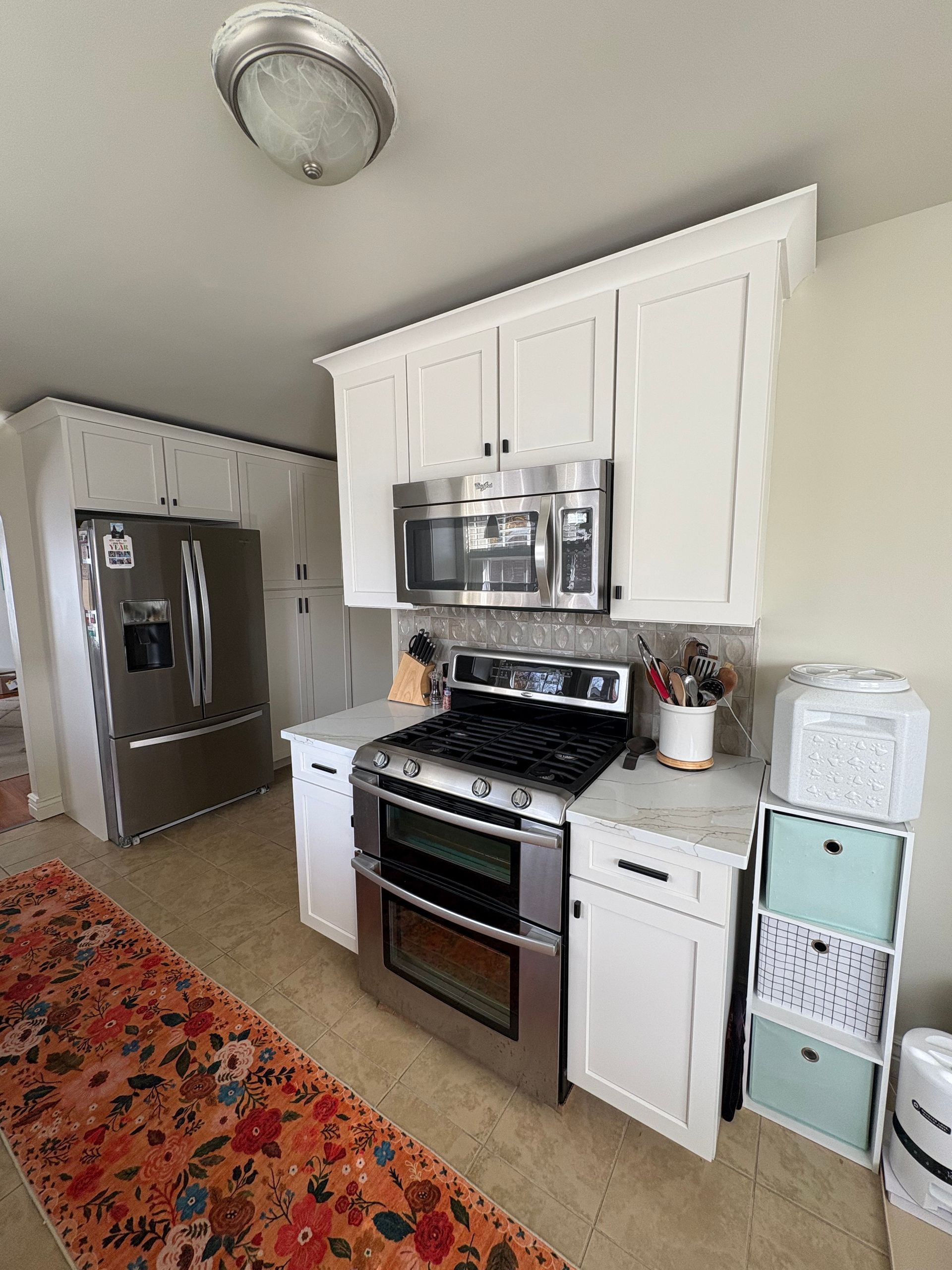 A kitchen with white cabinets, stainless steel appliances, and a colorful runner rug.