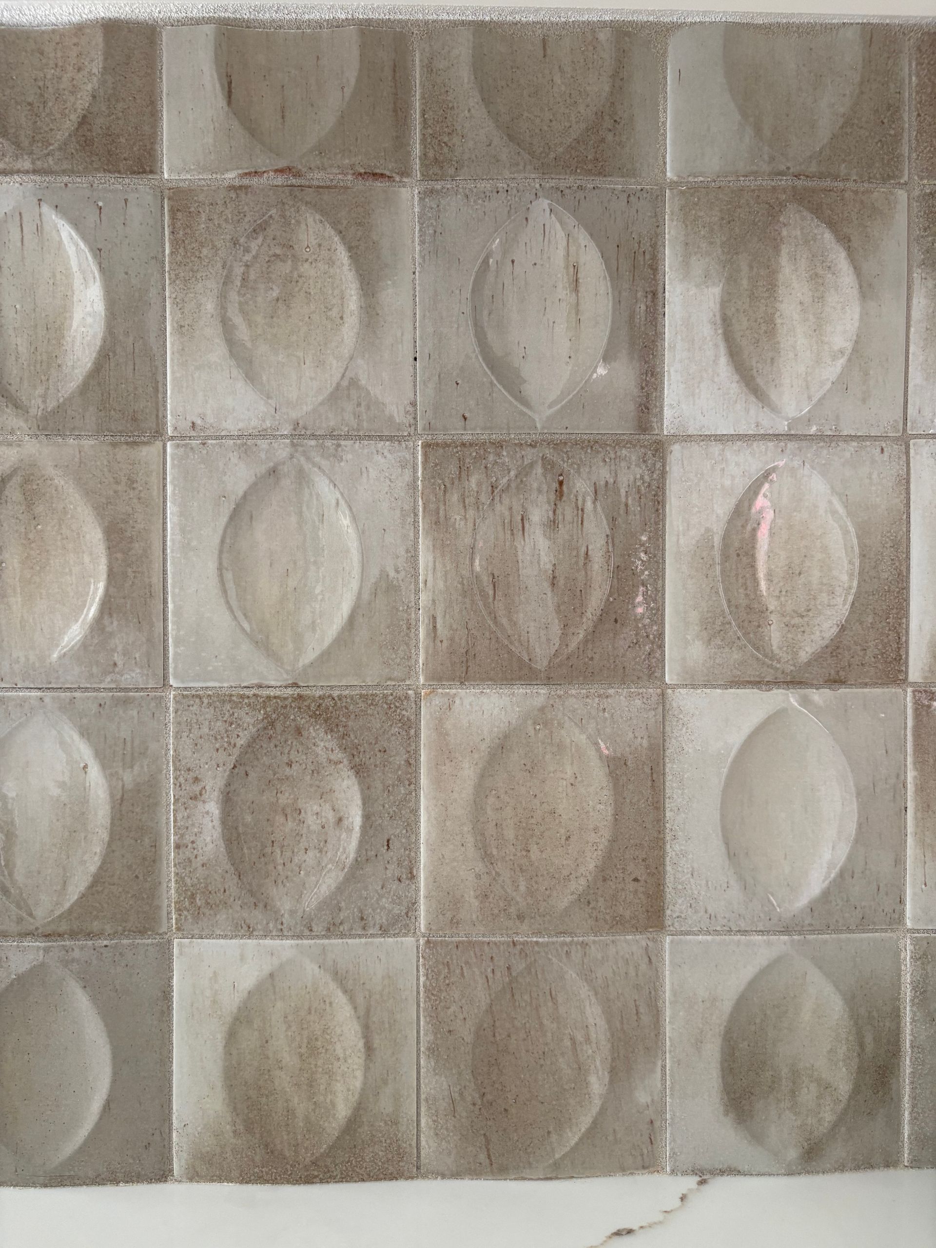 Gray and beige square wall tiles with a raised oval pattern.