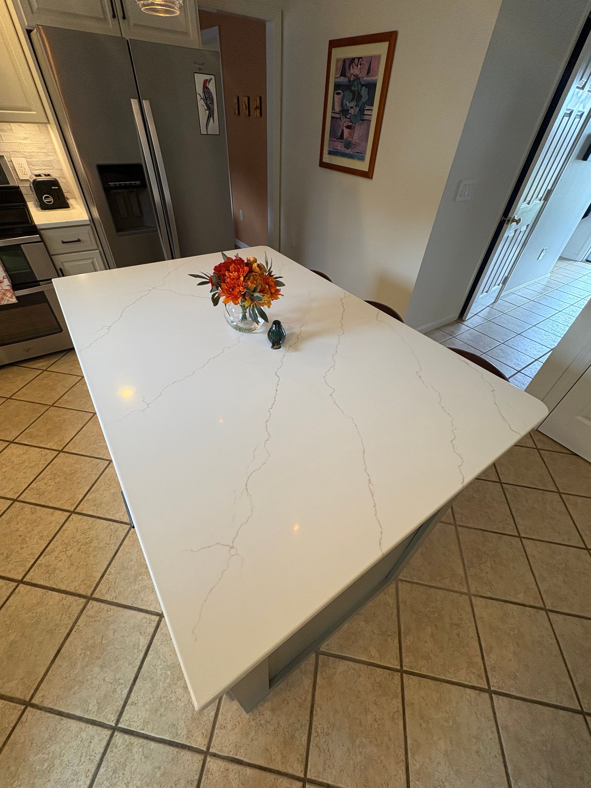 White kitchen island with flowers, tile floor, and refrigerator in the background.
