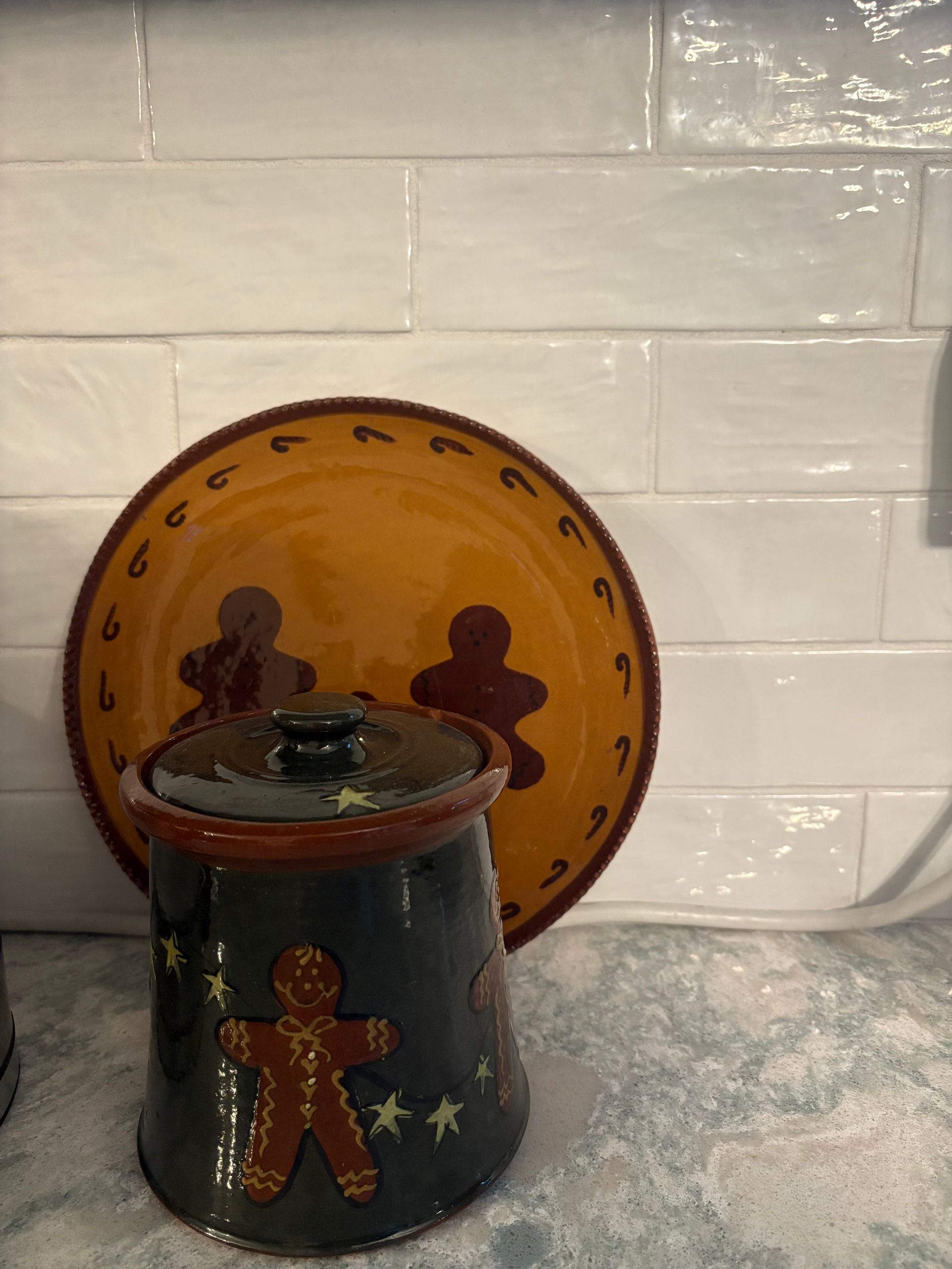 Gingerbread-themed ceramic jar with lid and plate on a light-colored countertop against a white tiled wall.