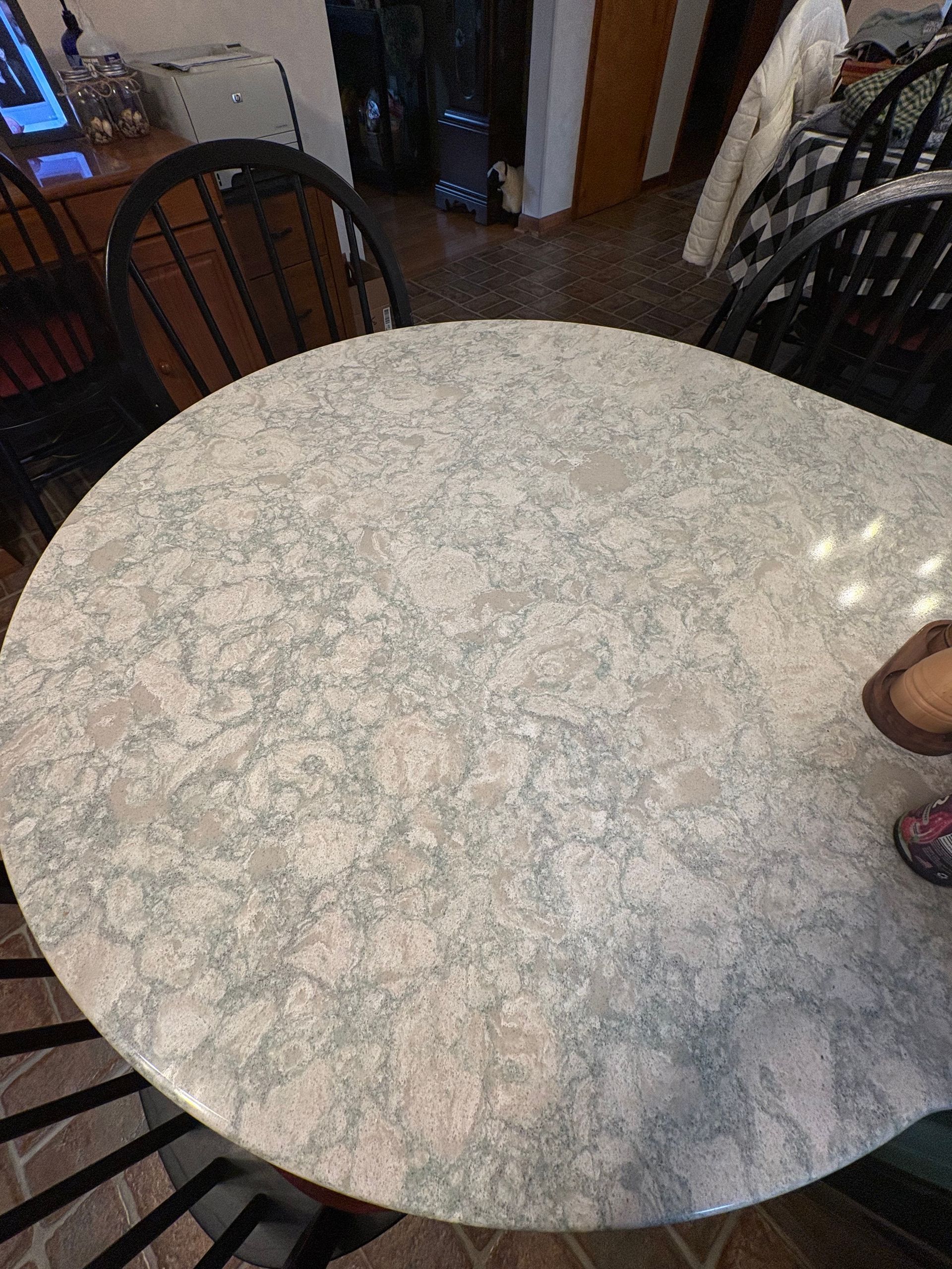 Overhead view of a round table with a speckled, light gray surface, surrounded by black chairs.