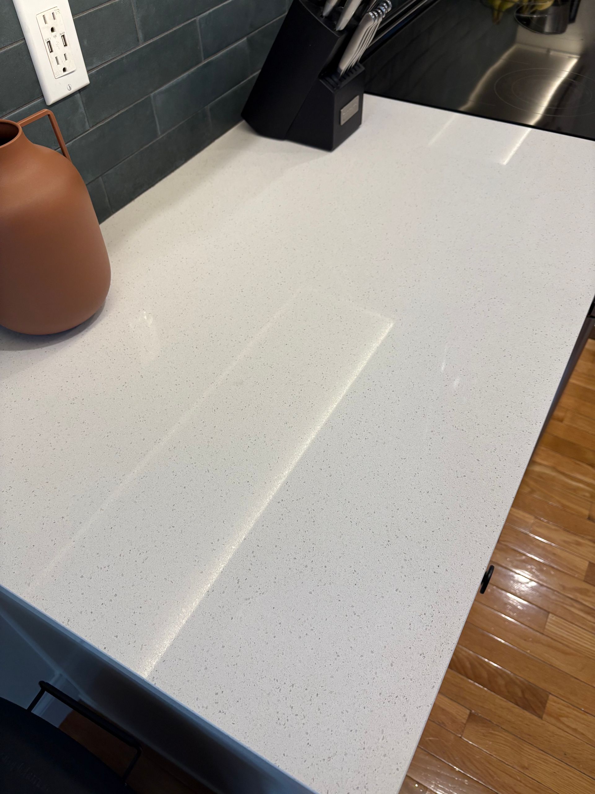 White speckled quartz countertop with terracotta vase, knives, and blue-grey backsplash.