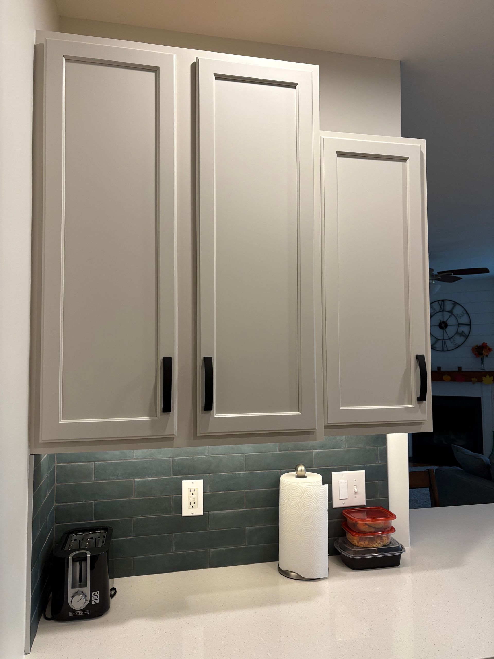 Gray kitchen cabinets with black handles above a countertop with a tiled backsplash.