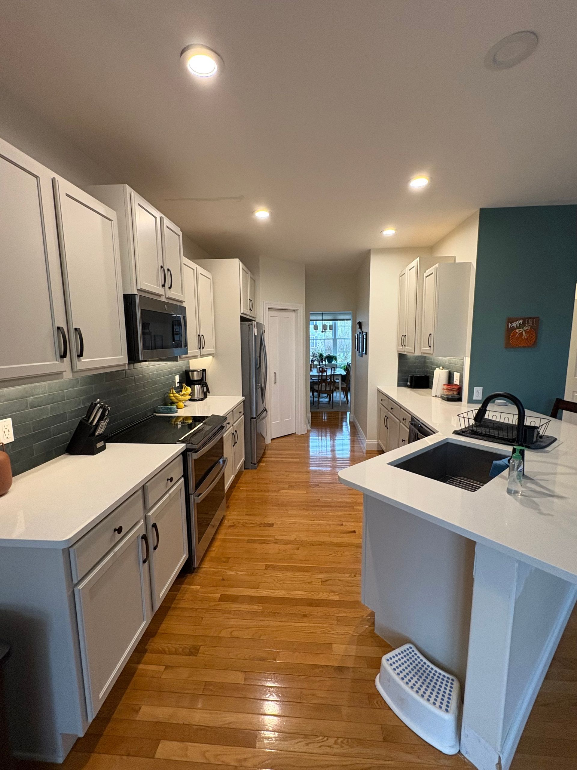 Modern kitchen with white cabinets, stainless steel appliances, and wooden floors.