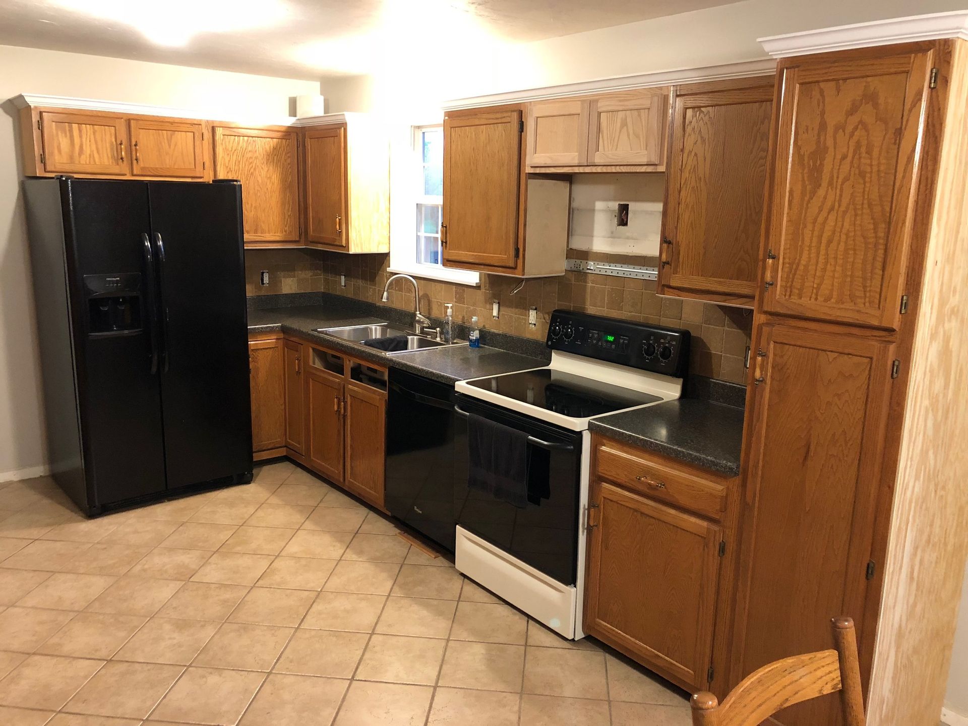 Kitchen with wood cabinets, black appliances, dark countertops, and beige tile floor.