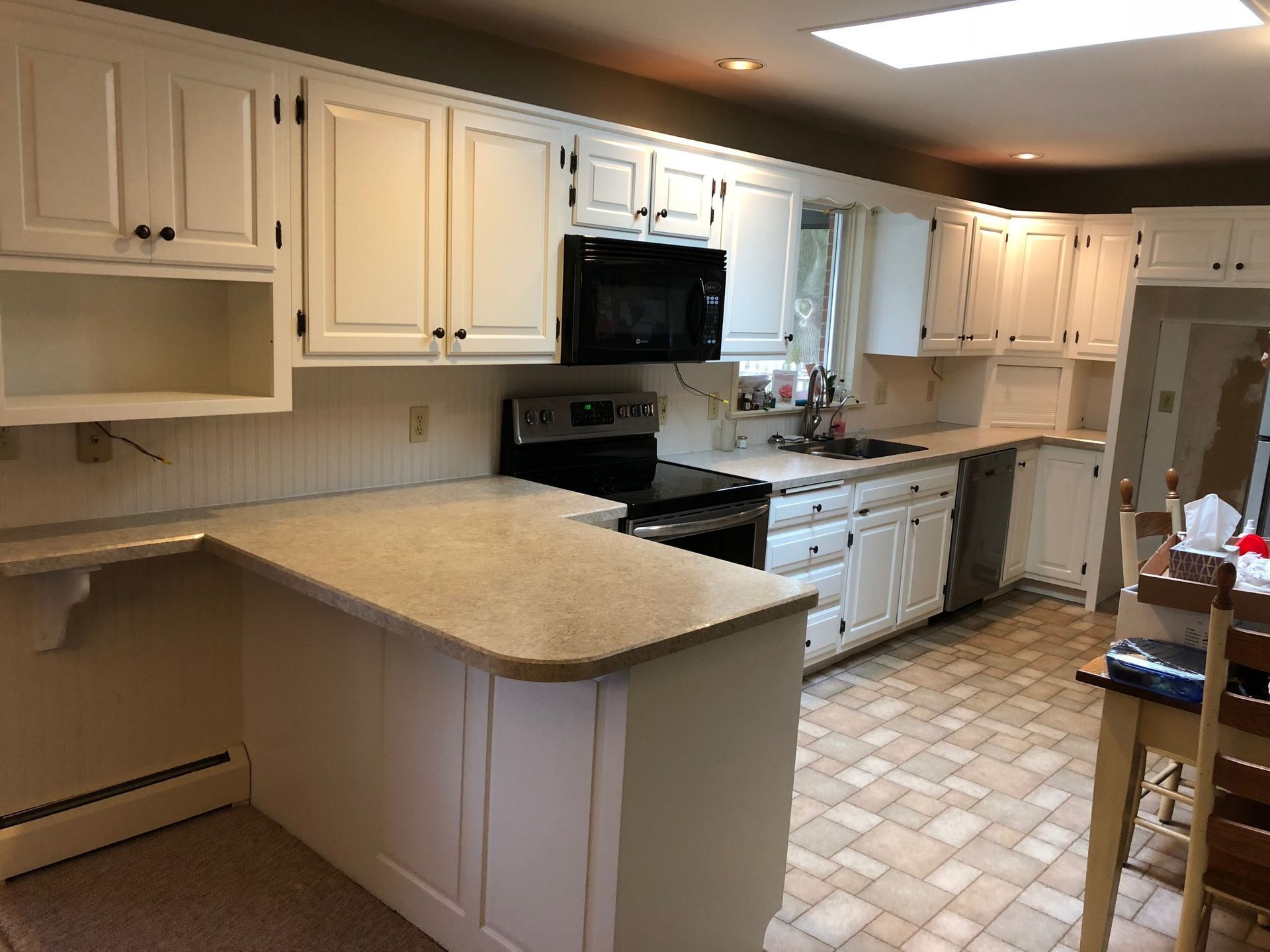 White kitchen cabinets and countertops; black appliances, tile floor.