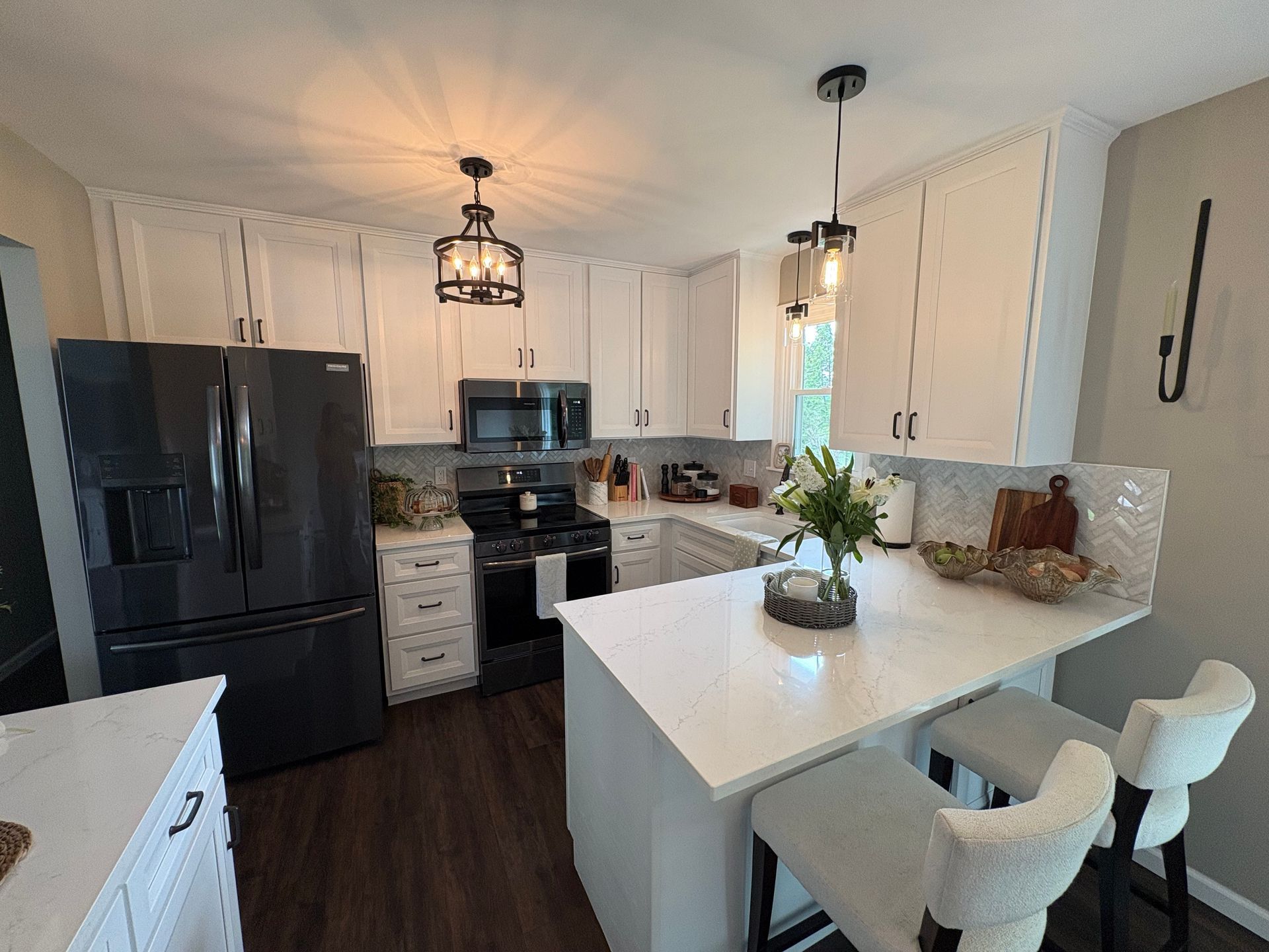 Bright modern kitchen with black appliances, white island, and two barstools under pendant lights