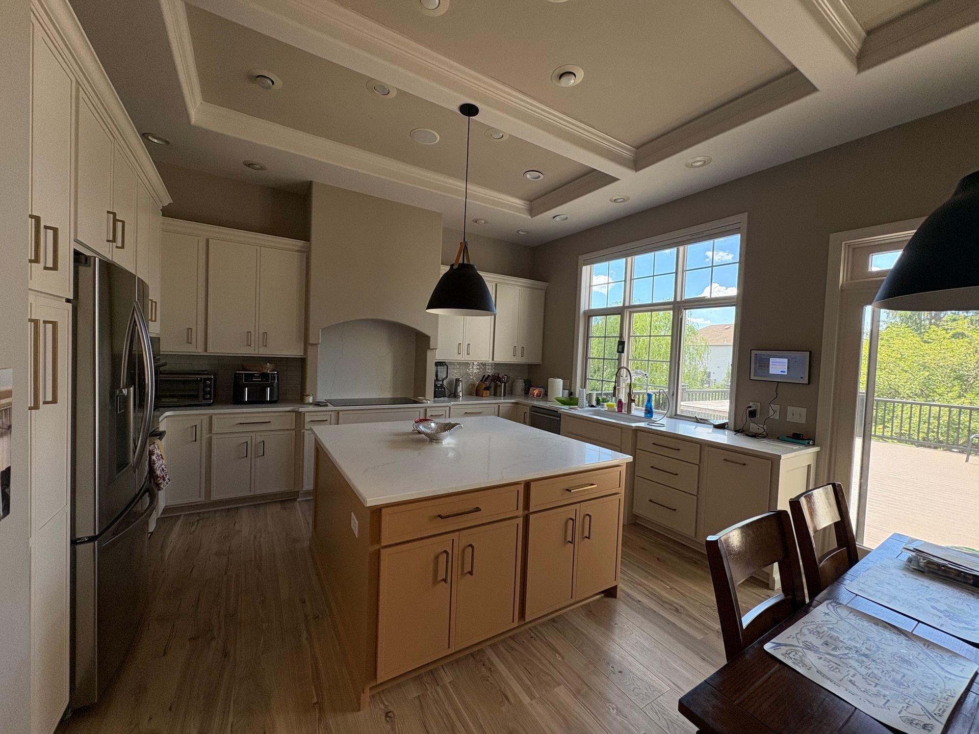 Bright modern kitchen with a center island, white cabinets, pendant lights, and large window overlooking greenery