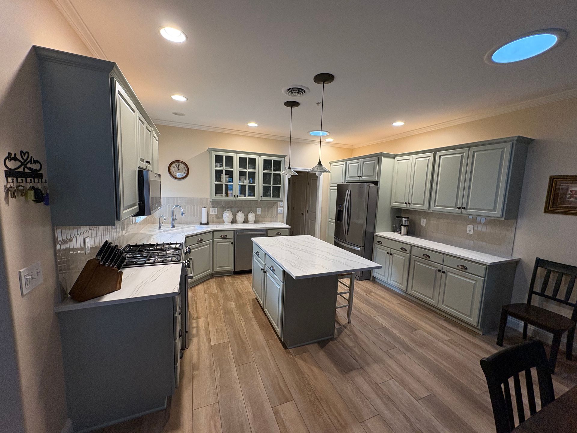 Bright modern kitchen with gray cabinets, white island, wood floors, and recessed lighting