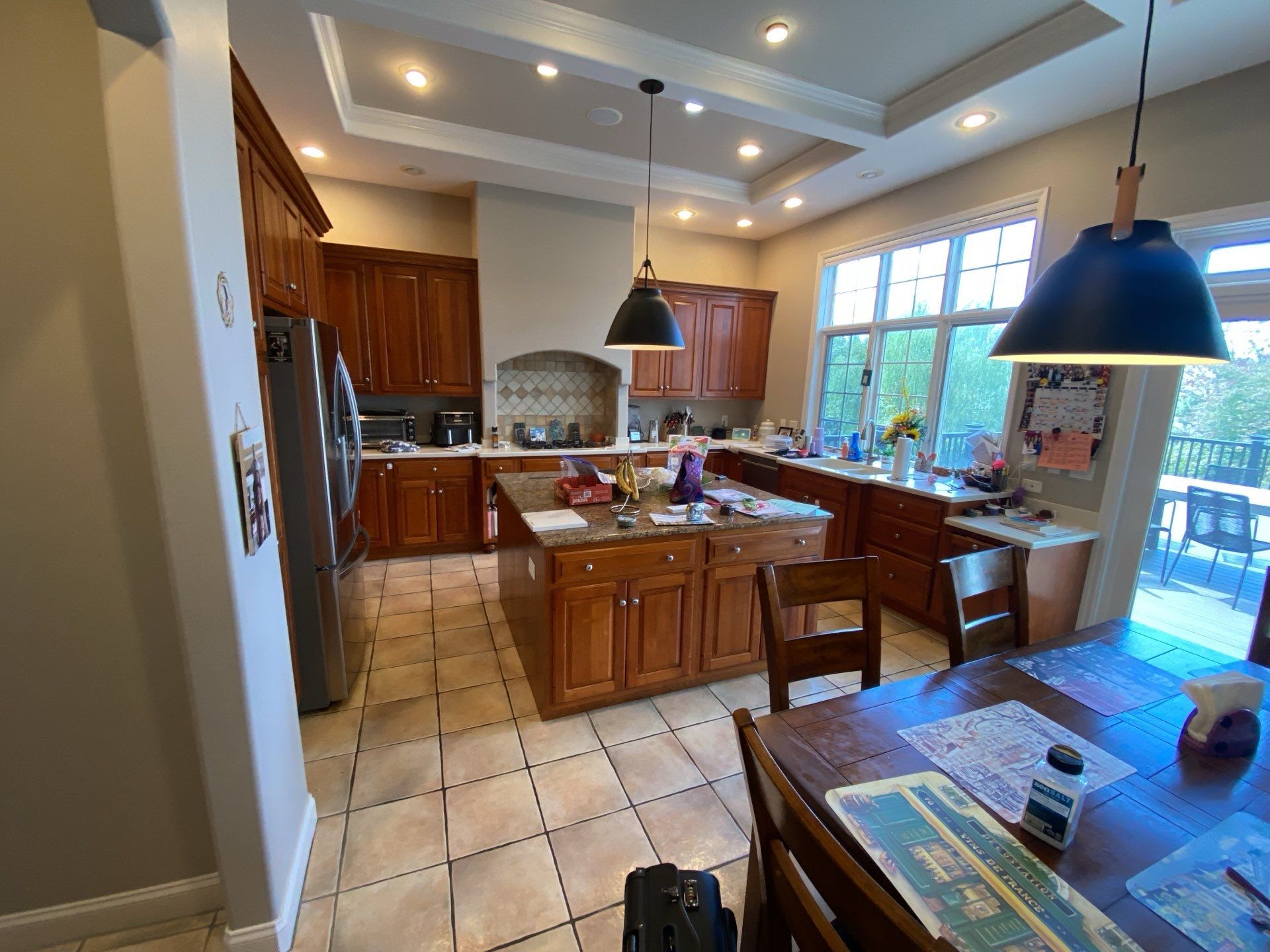 Spacious kitchen with wooden cabinets, tiled floor, island, and large windows letting in daylight
