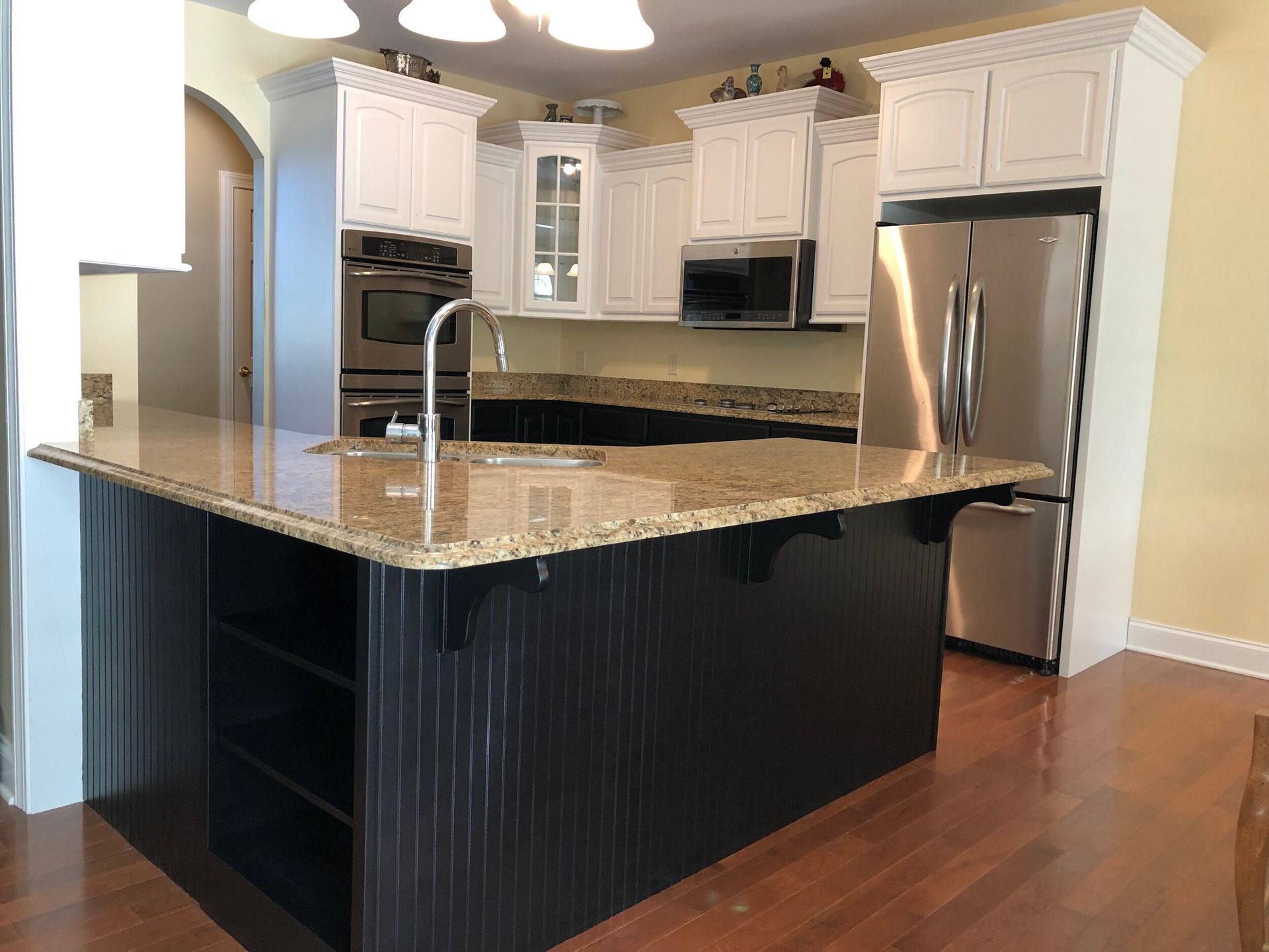 Kitchen with black island, granite countertop, white cabinets, stainless steel refrigerator, and hardwood floor.
