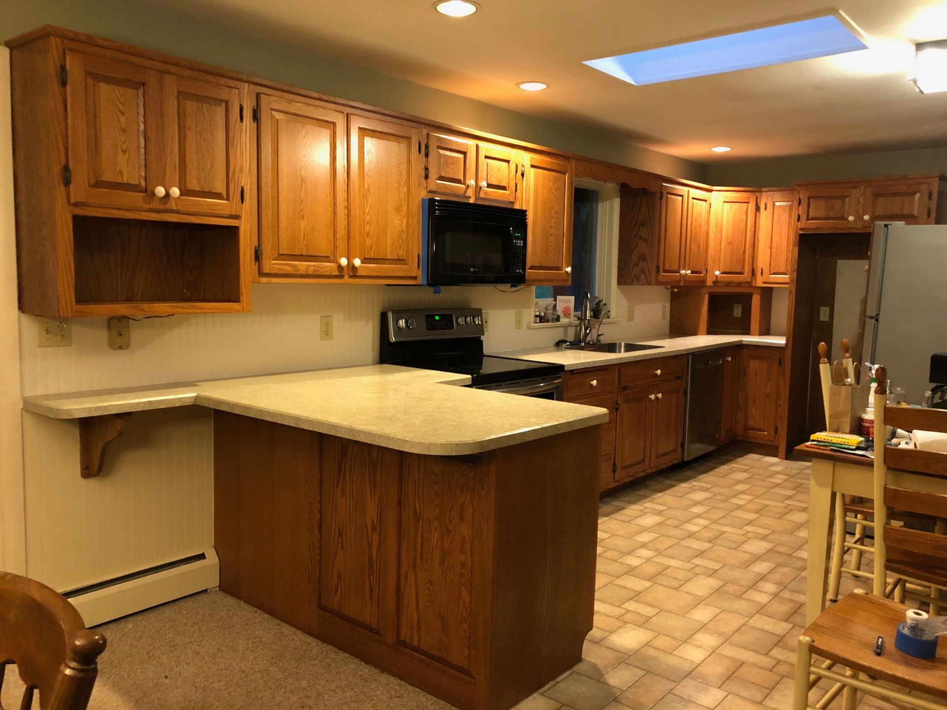 Oak kitchen cabinets and island with beige countertop and tile floor.