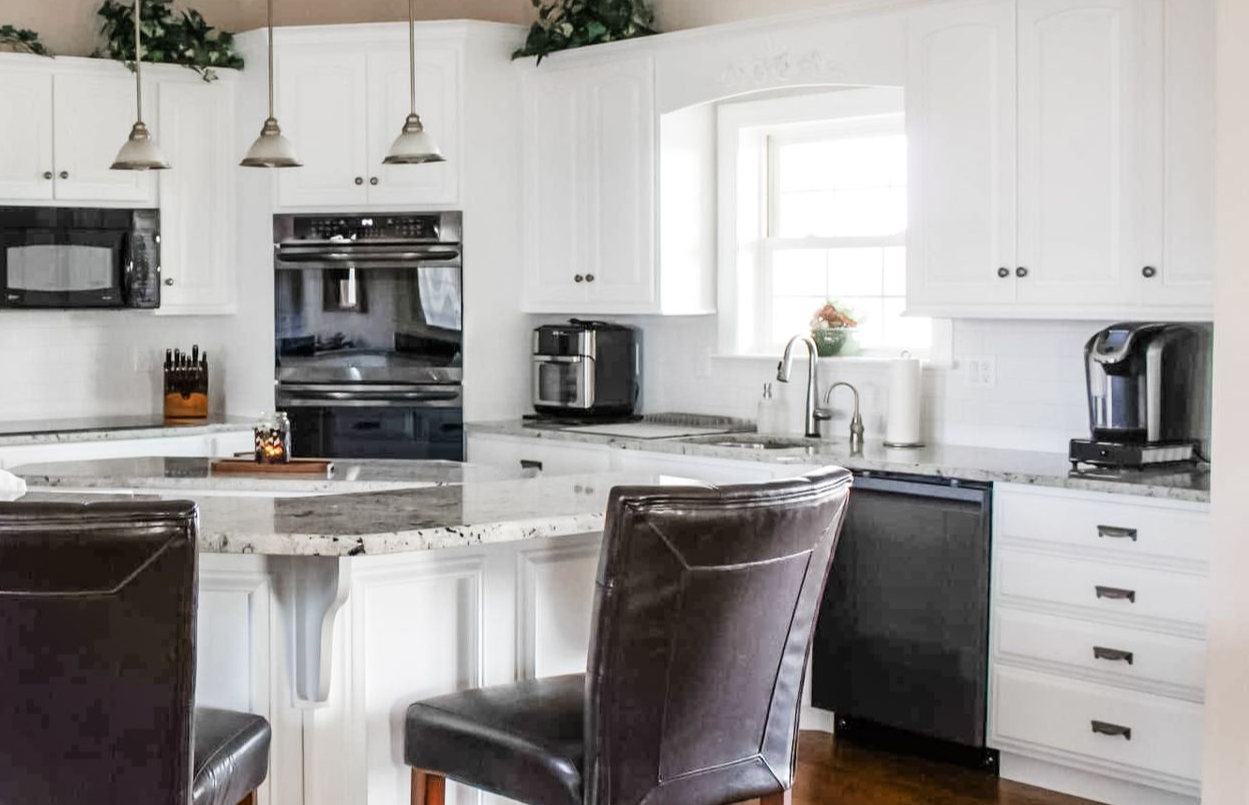 White kitchen with a breakfast bar, featuring black appliances and leather bar stools.
