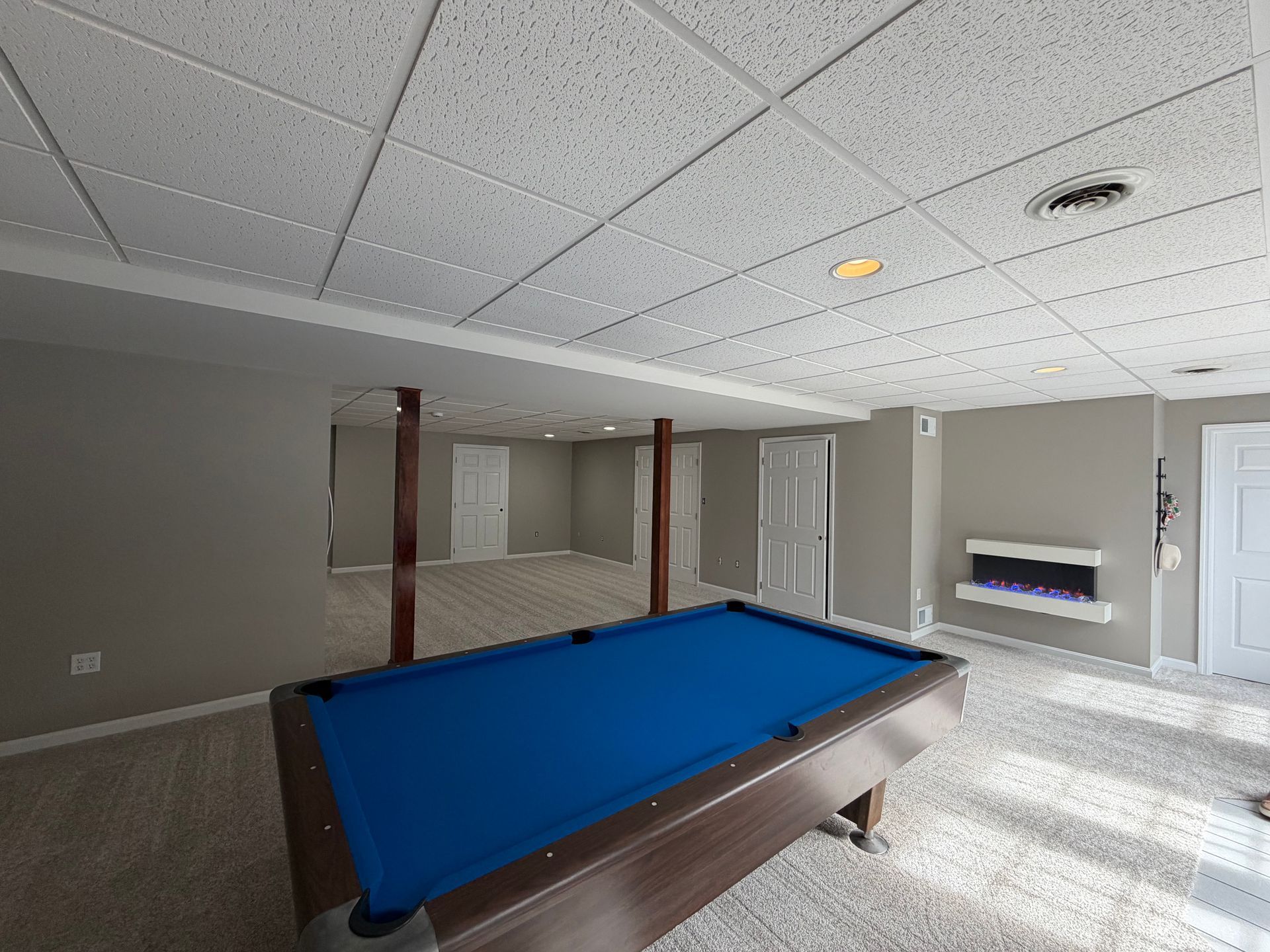 Basement rec room with blue-felt pool table, carpet, and fireplace in neutral tones