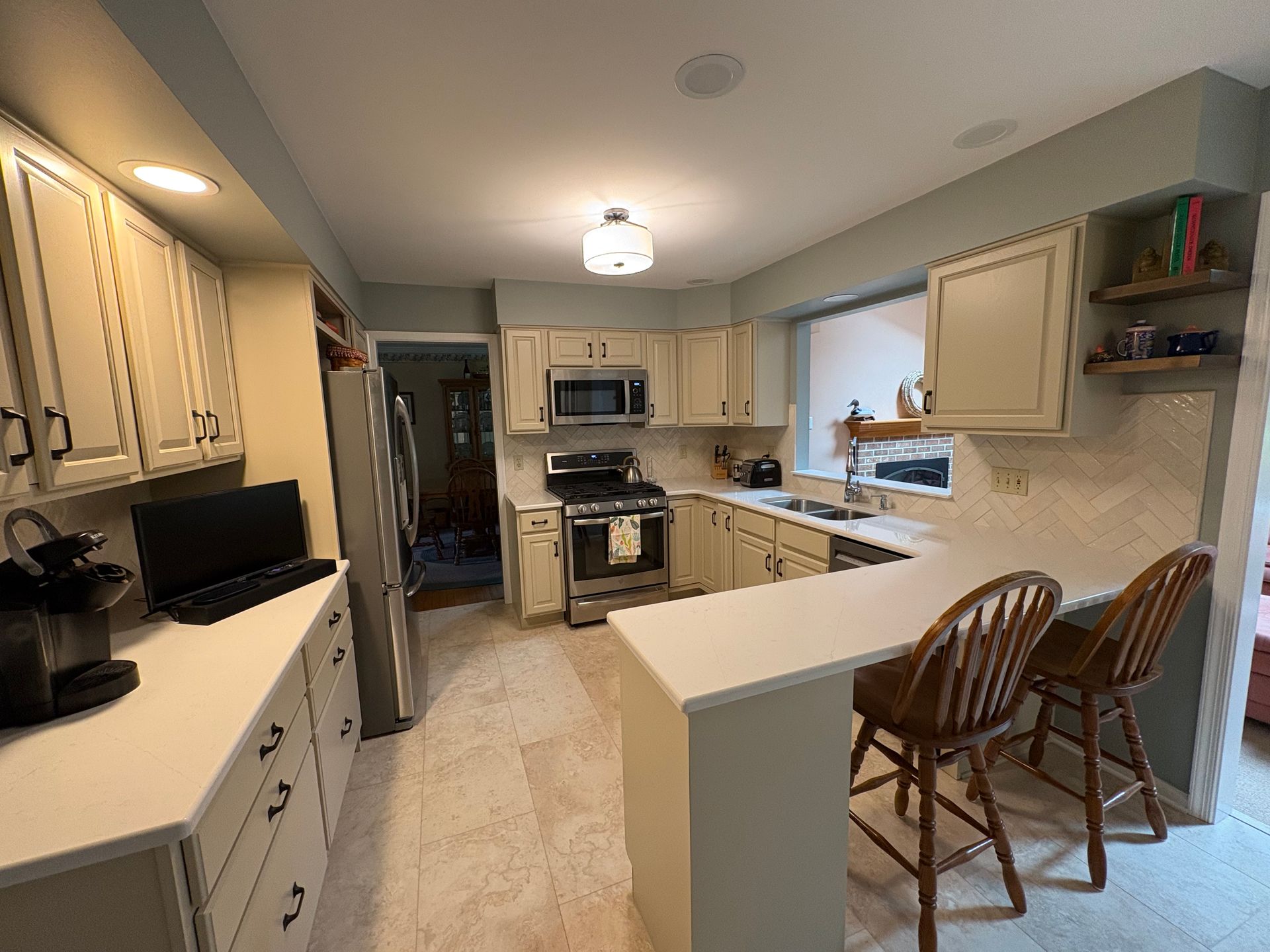 Bright kitchen with white cabinets, stainless appliances, and two wooden stools at a breakfast bar.