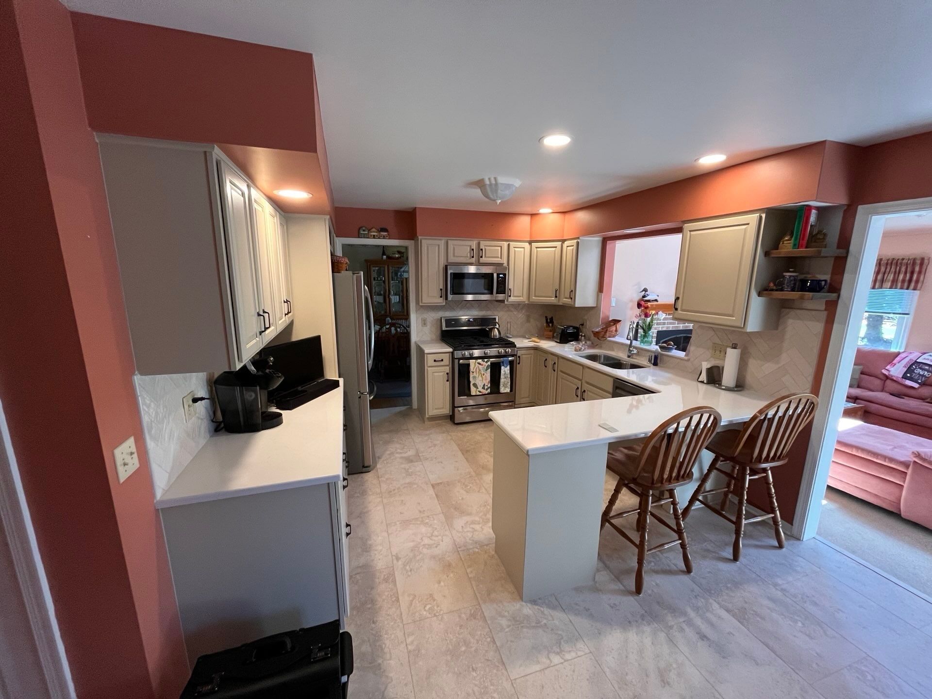 Open kitchen with island, stainless appliances, red walls, and two wooden chairs by a bright window.