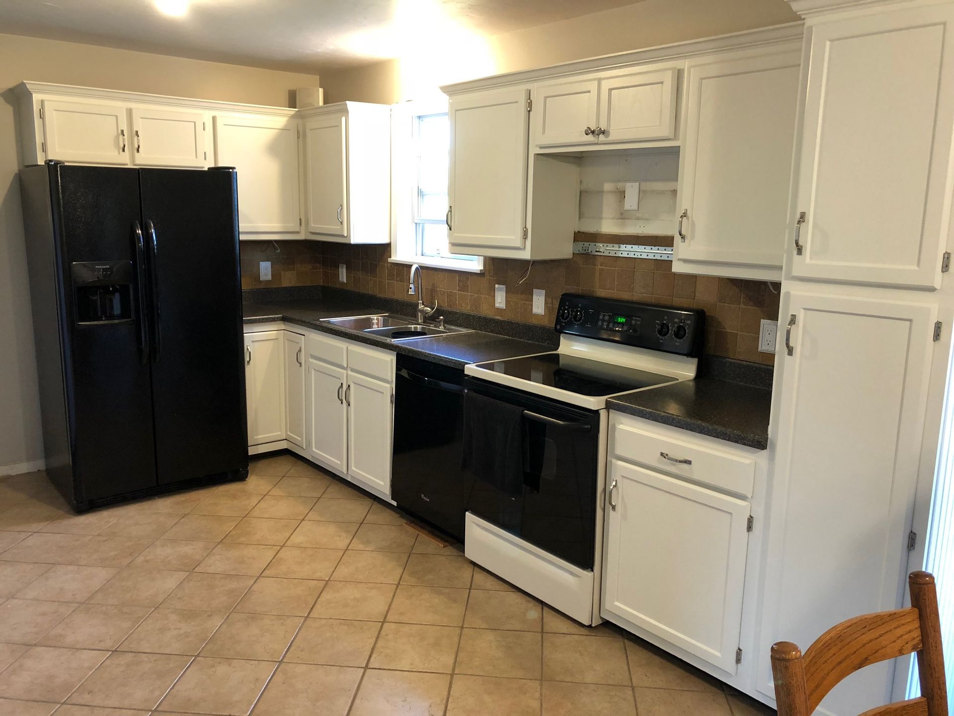 White kitchen cabinets with black appliances and countertops; tiled floor.