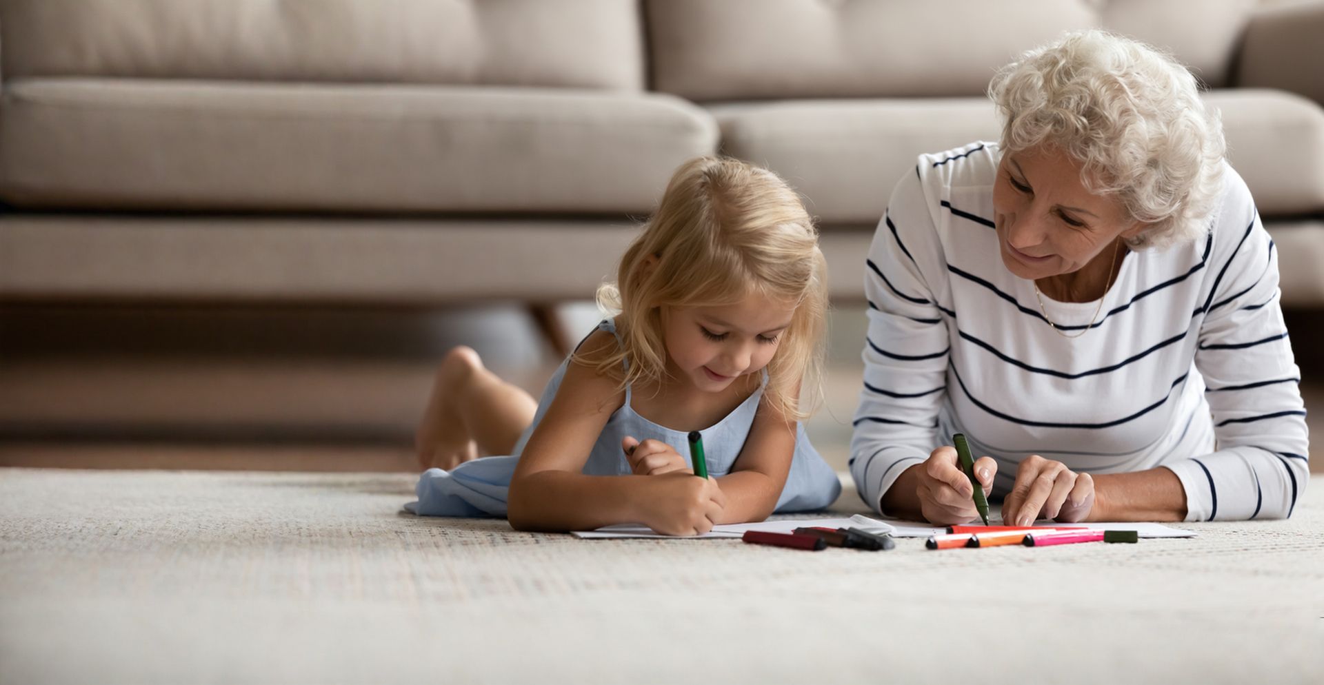 Woman and child drawing together on floor near sofa.