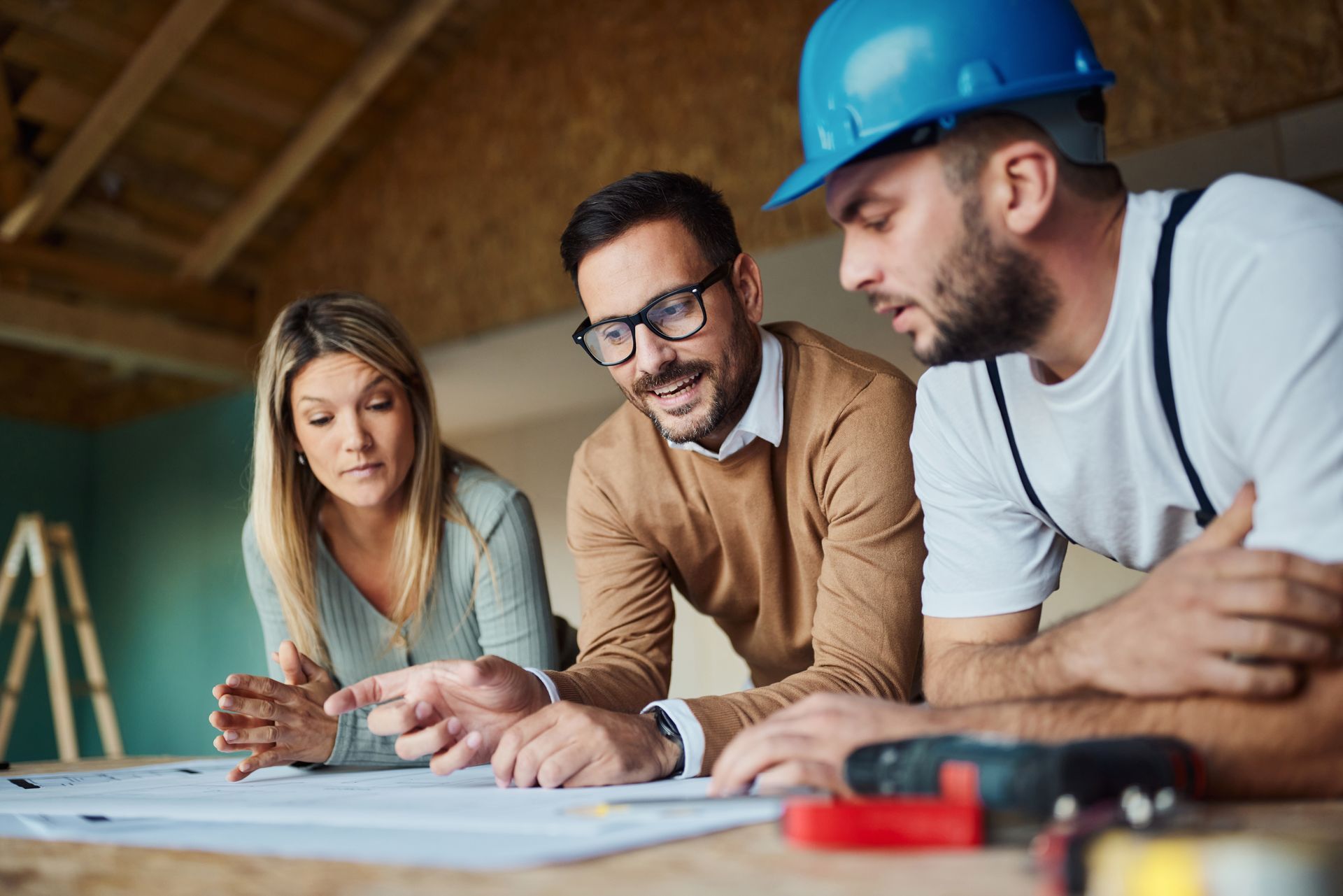 Couple and contractor reviewing blueprints at a construction site.