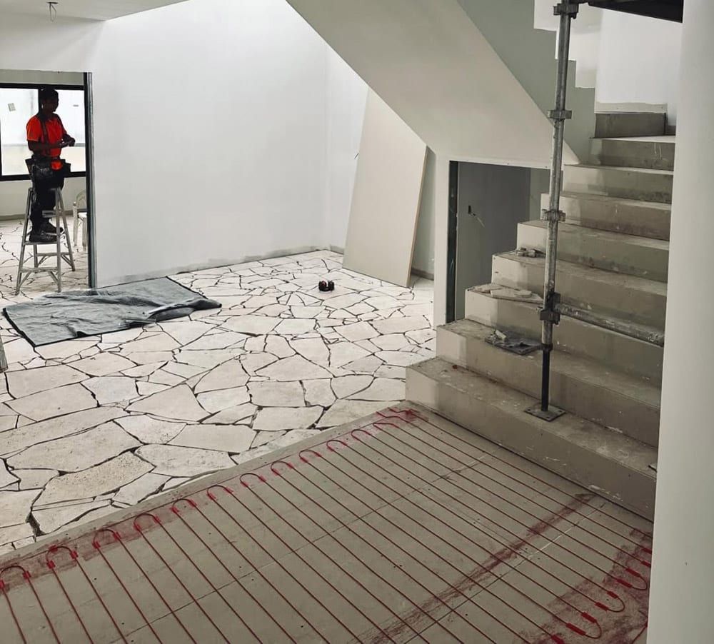 Stairwell interior with unfinished tiled floor, glass railing, and a worker in red at left.
