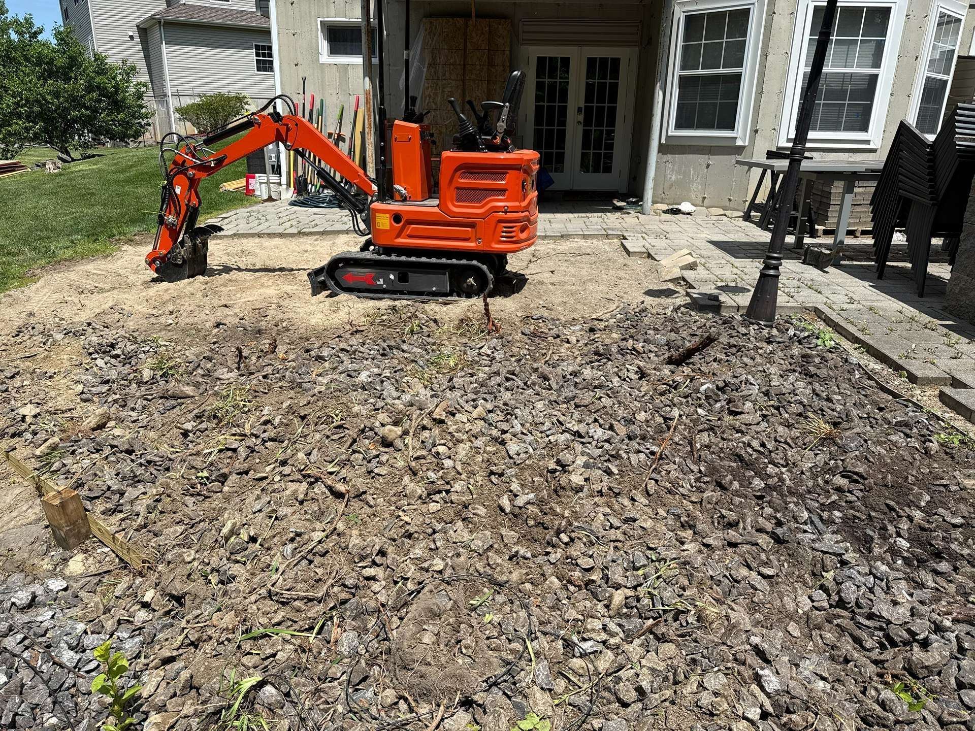 Orange mini excavator digging gravel in a residential yard beside a house
