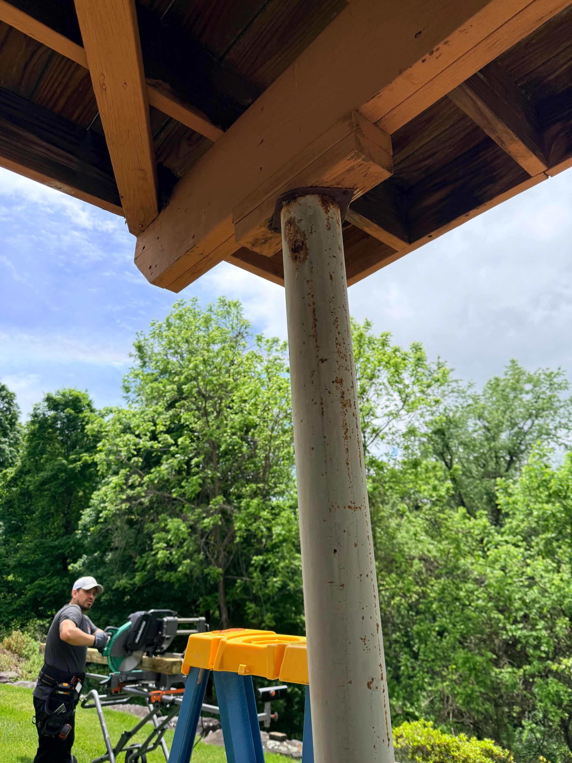 Person standing beside a green tractor under a wooden pavilion, with trees in the background