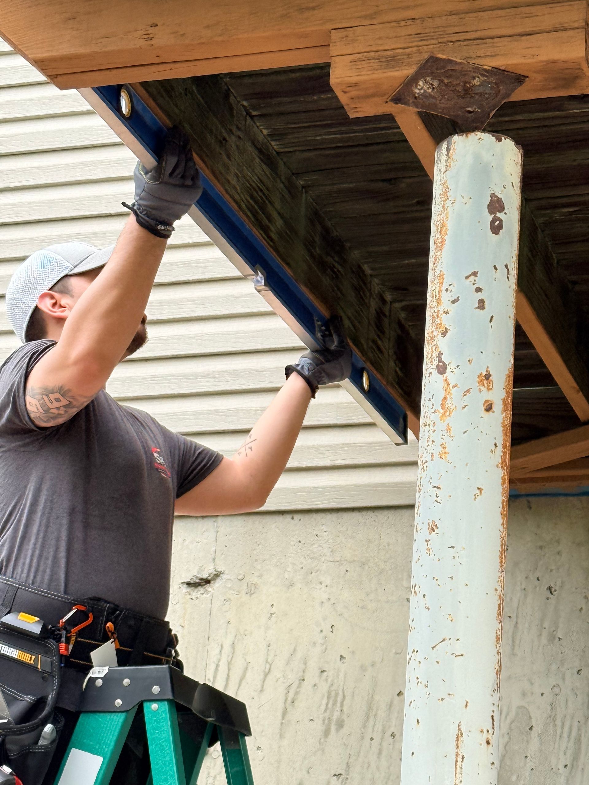 Worker installing soffit panels under a roof overhang, wearing gloves beside a white support post.
