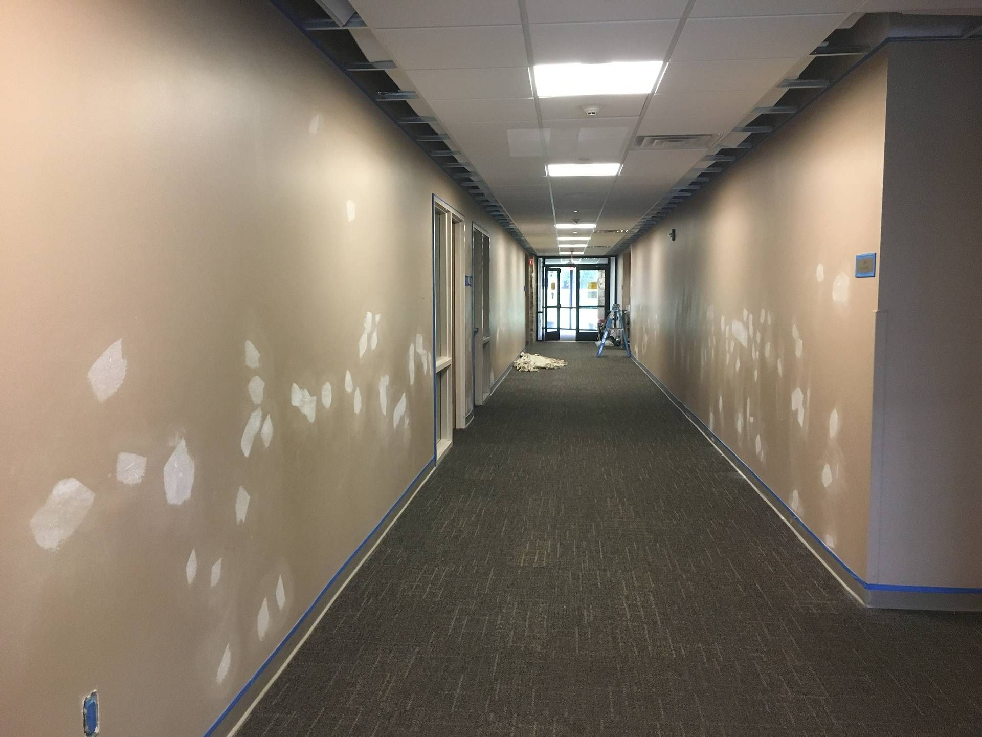 Empty indoor hallway with beige walls, dark carpet, and a bright doorway at the end