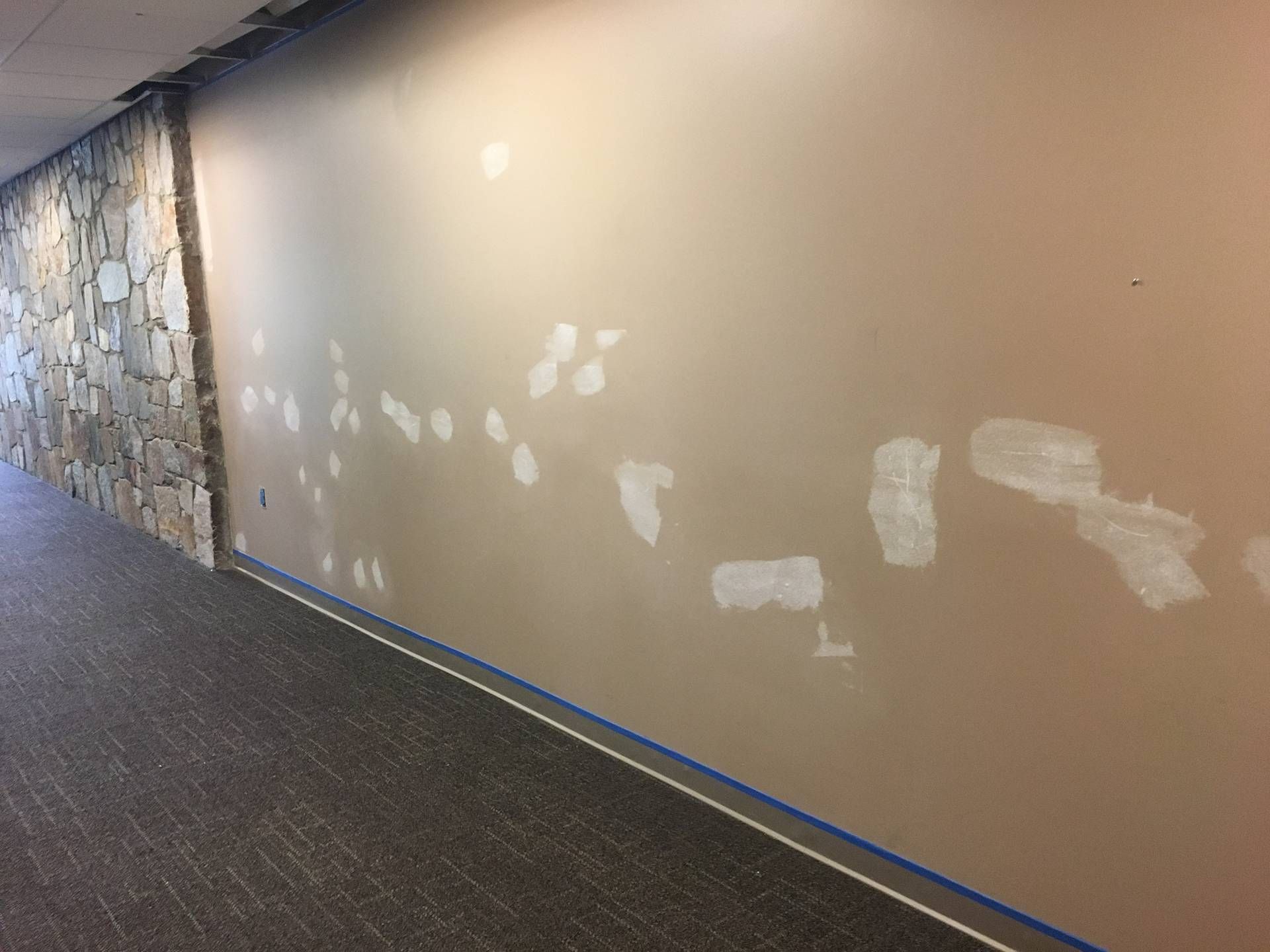 Empty hallway with beige wall showing white paint patches and a stone accent wall on the left
