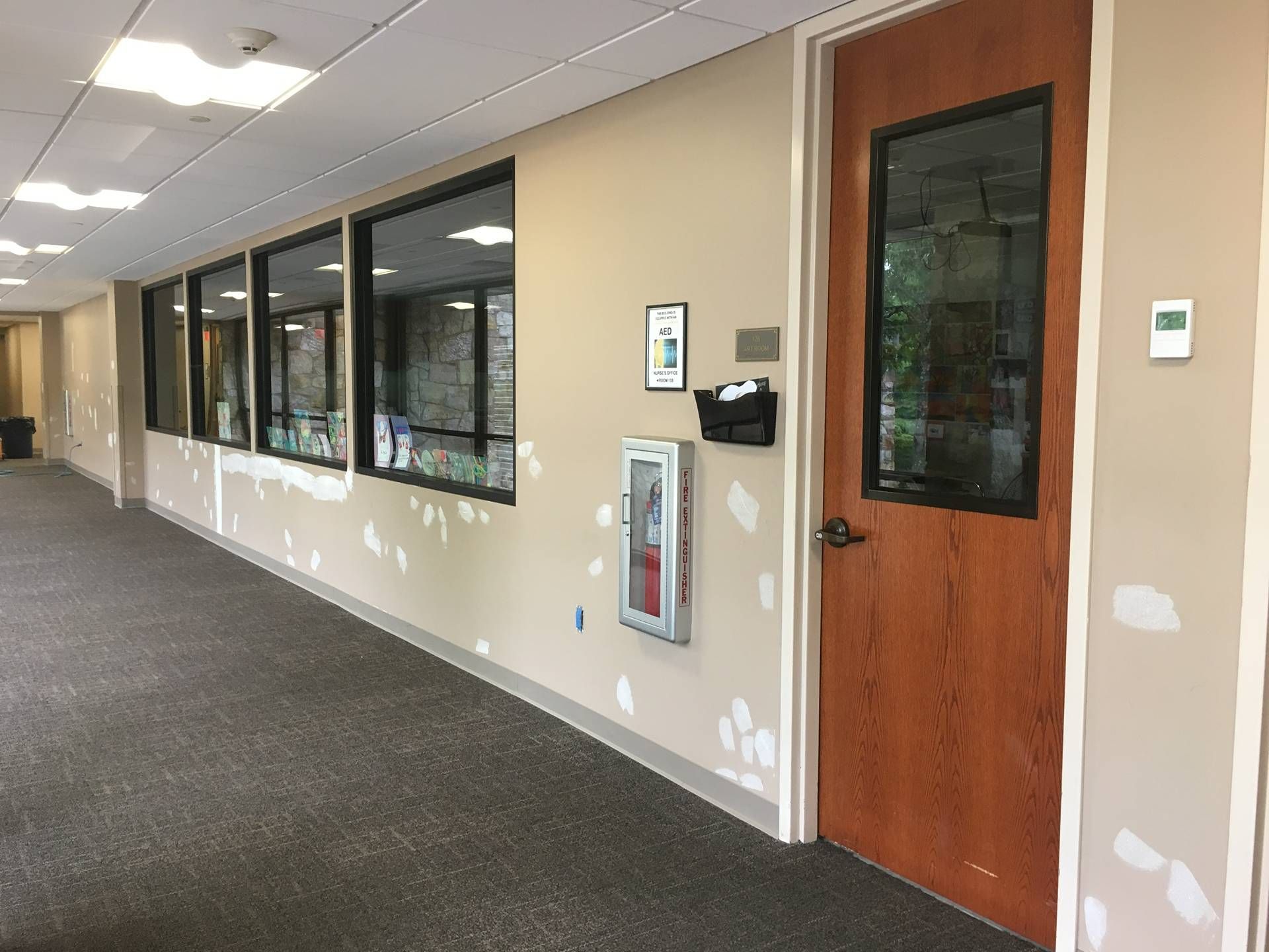 Hallway with carpet, windows, beige walls, and a wooden door with safety equipment mounted beside it