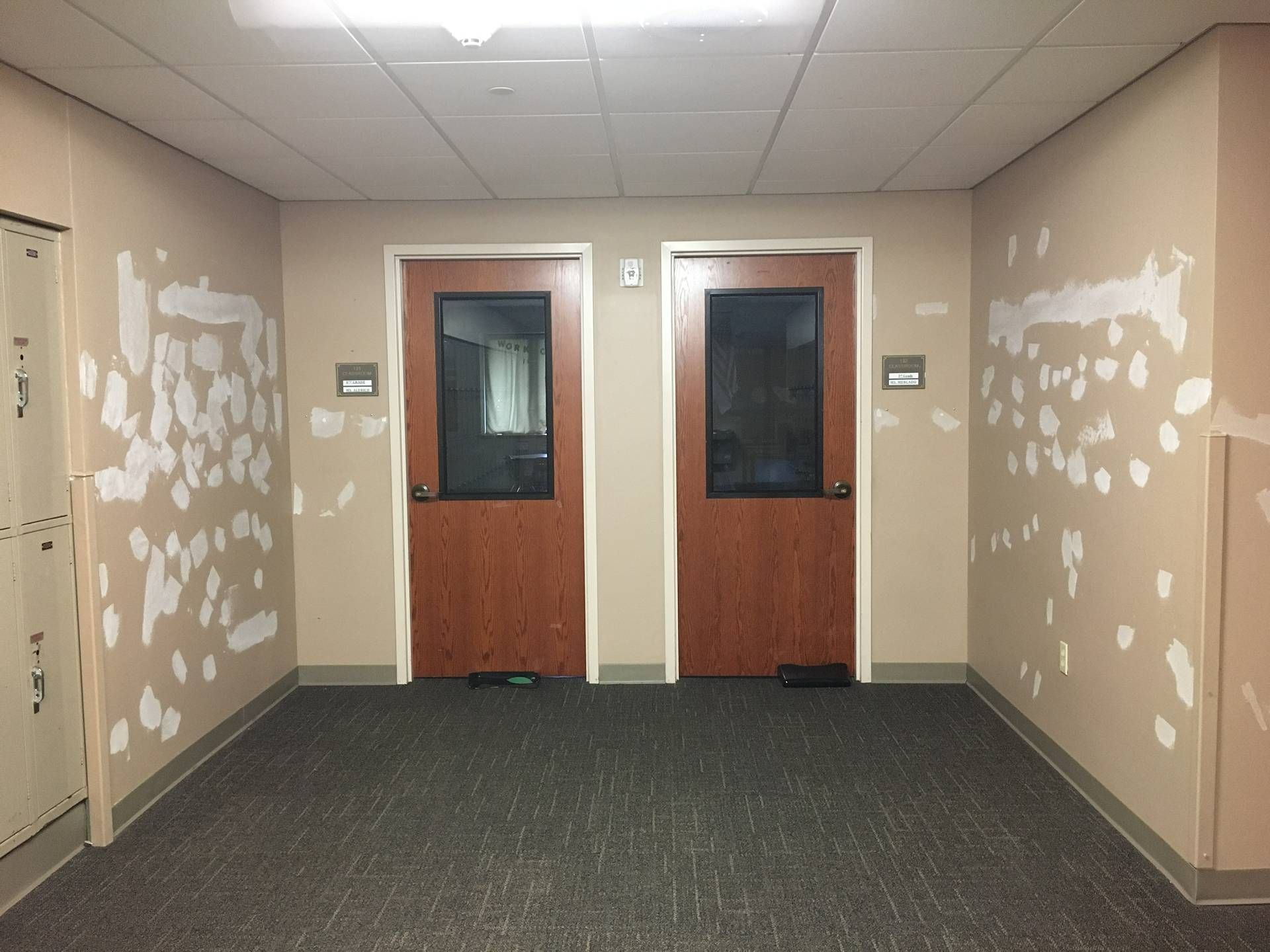Empty hallway with two wooden doors and white patchy walls, viewed from the carpeted end of the corridor