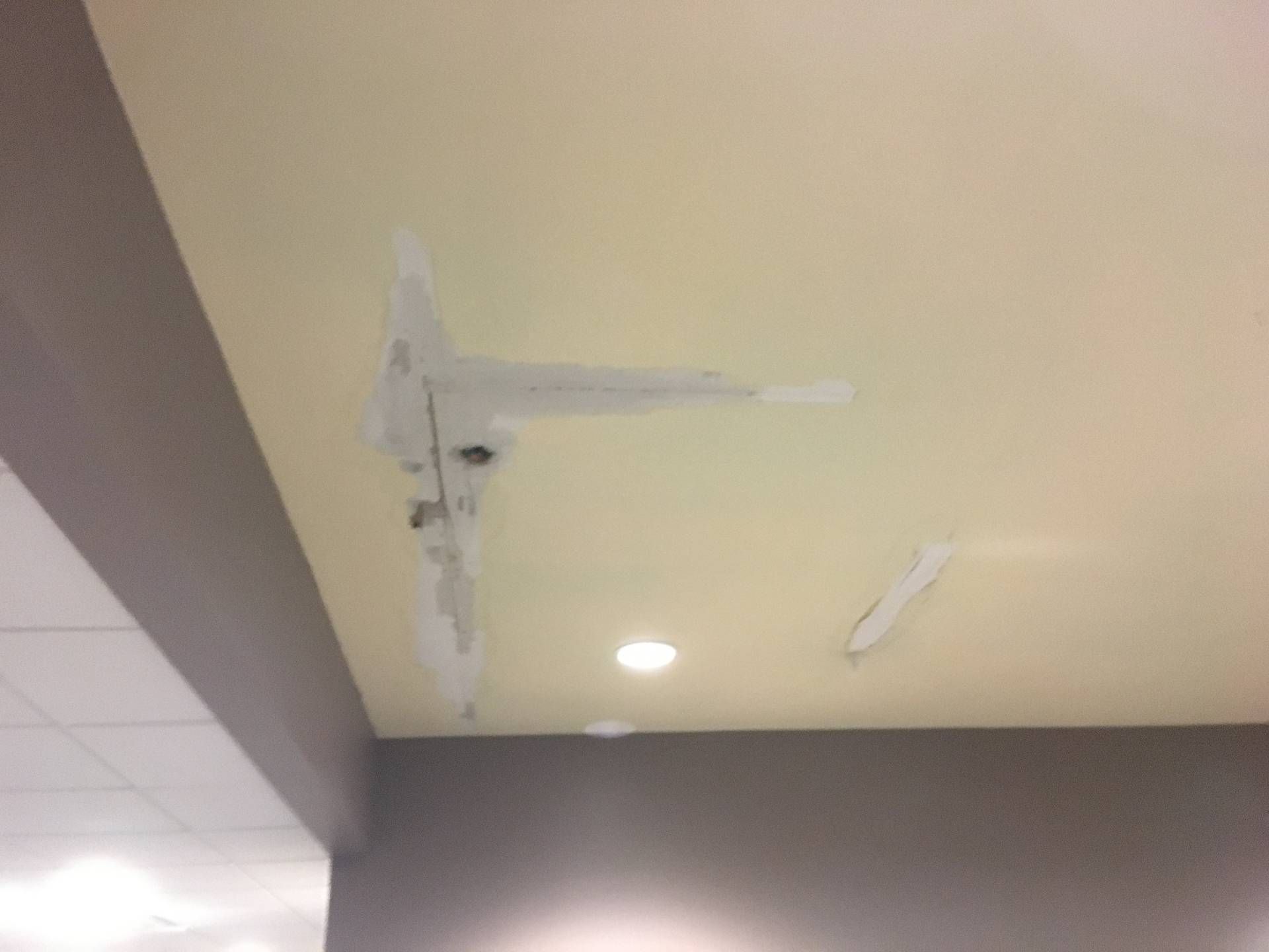 Ceiling with a loose, taped smoke detector and recessed light in a hallway
