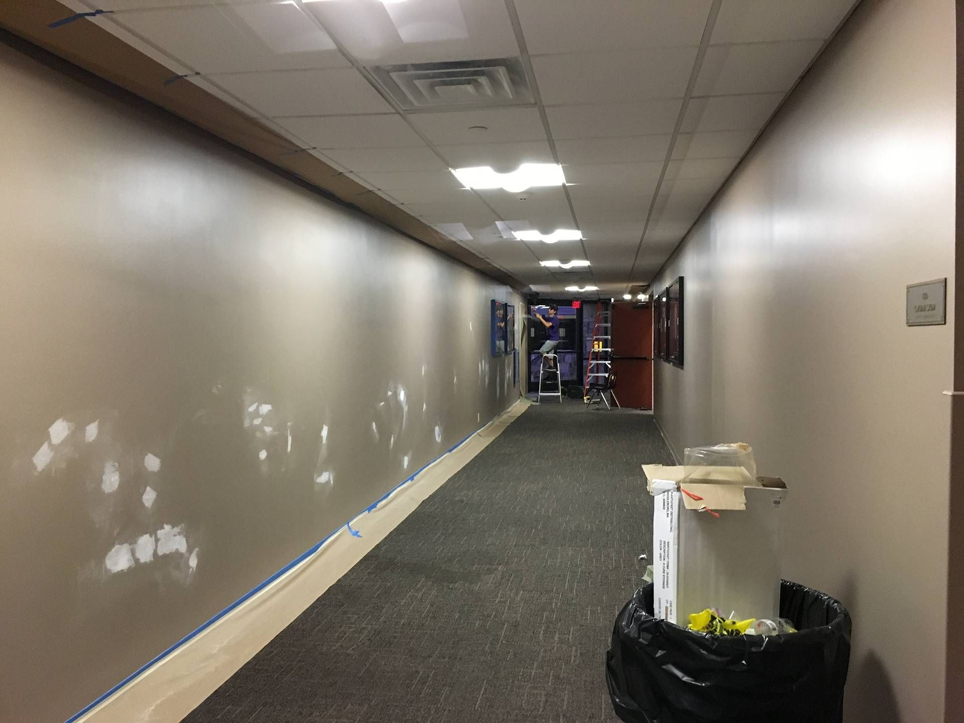 Long beige hallway with carpet, ceiling lights, and construction materials near the far end