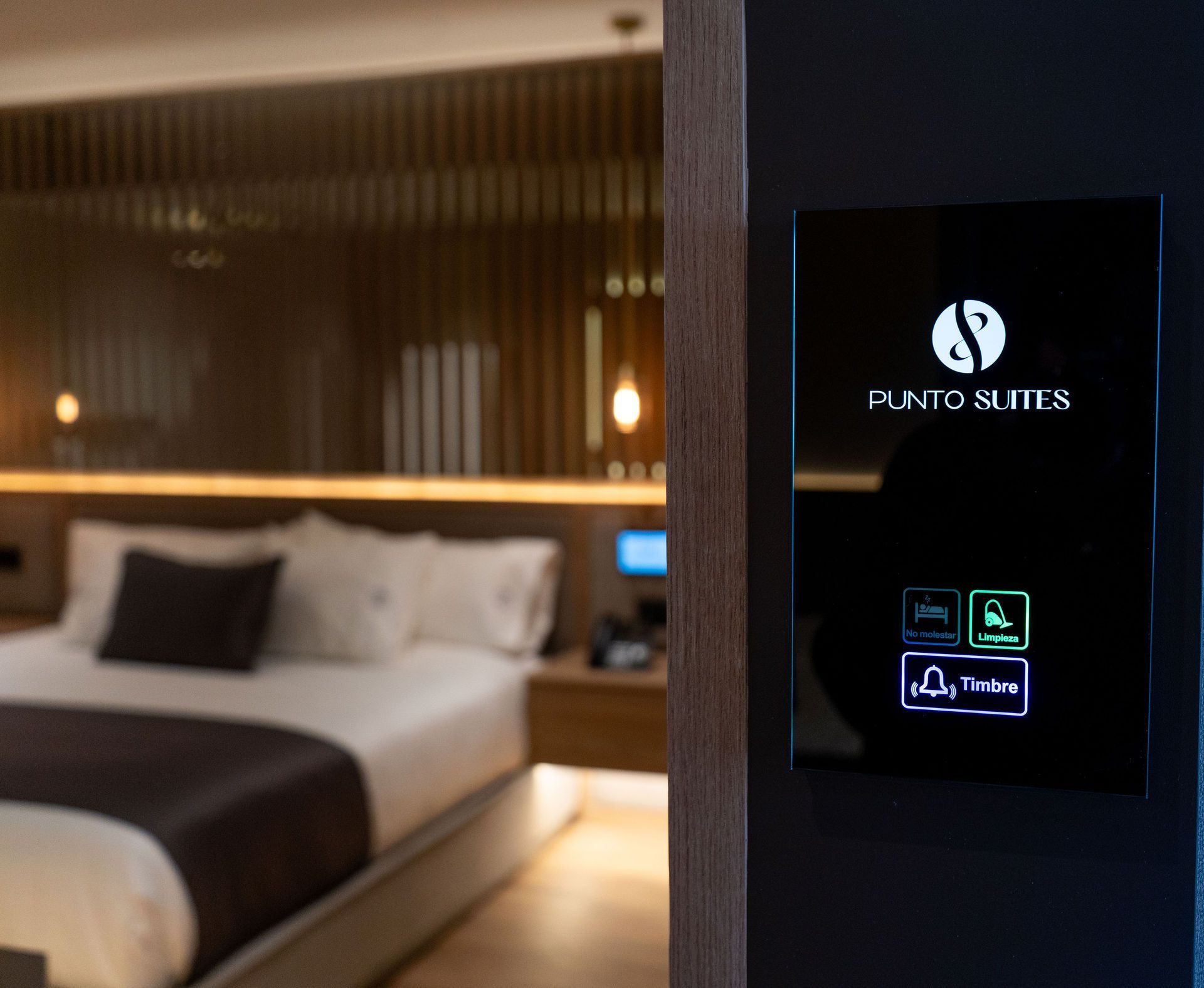 Una habitación del hotel Punto Suites que cuenta con un elegante panel de control junto a la cama con iconos iluminados para los servicios de la habitación.