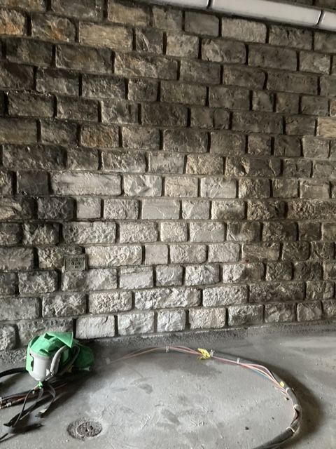 Mur en pierre avec un casque vert, un tuyau d'arrosage et un sol en béton dans une zone de construction