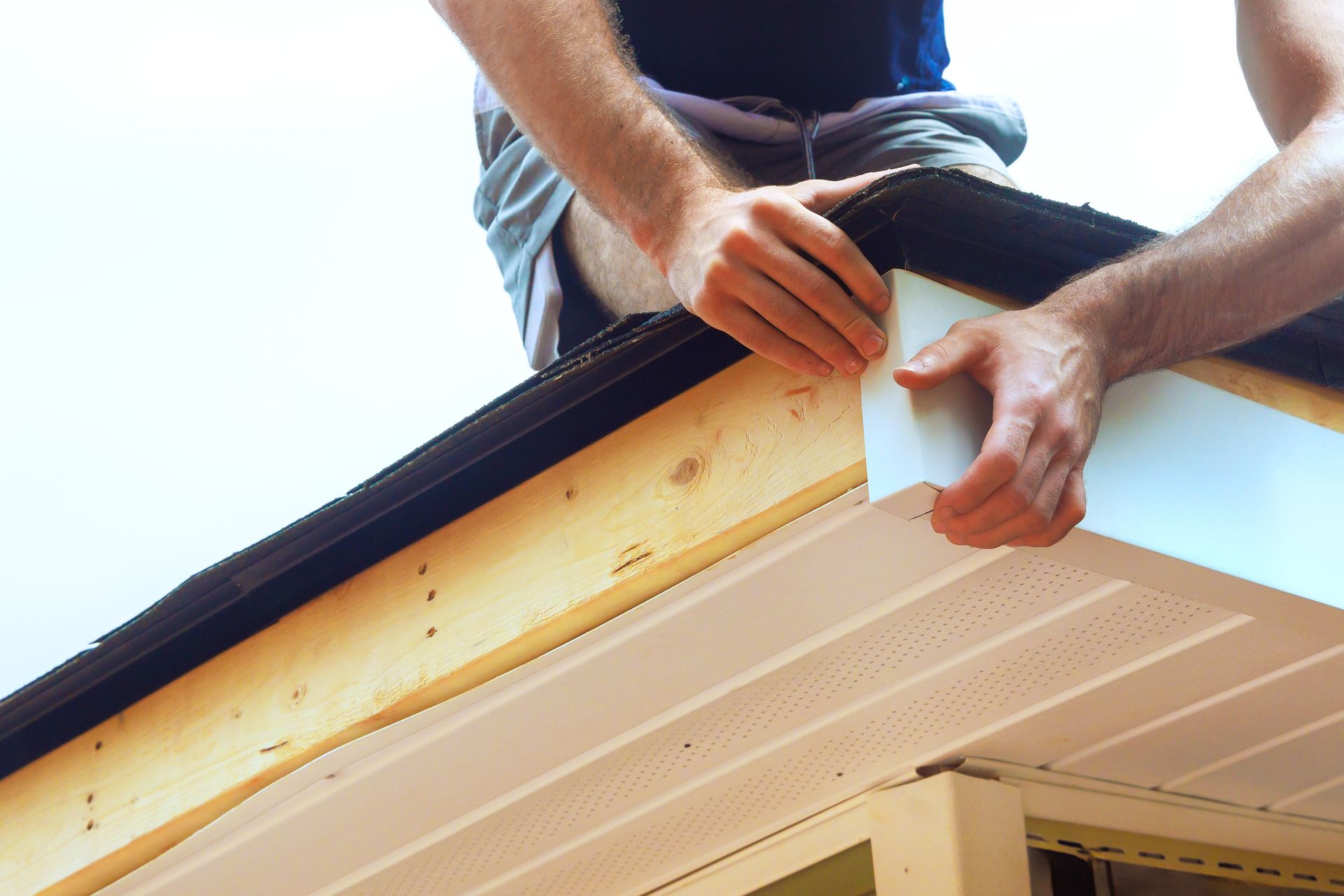 A person installs white fascia board onto the wooden edge of a roof,