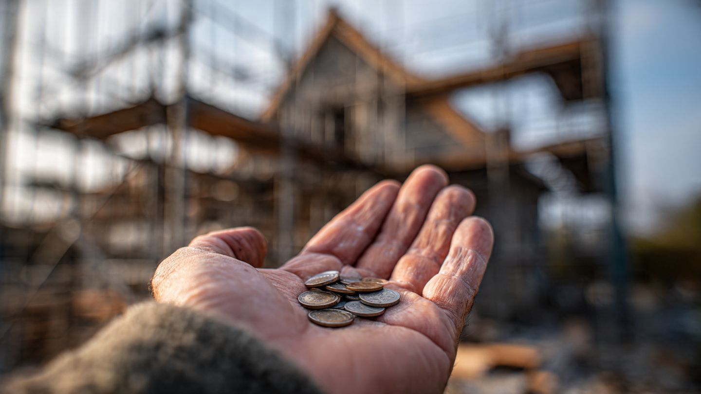 Hand holding coins in front of a house under construction