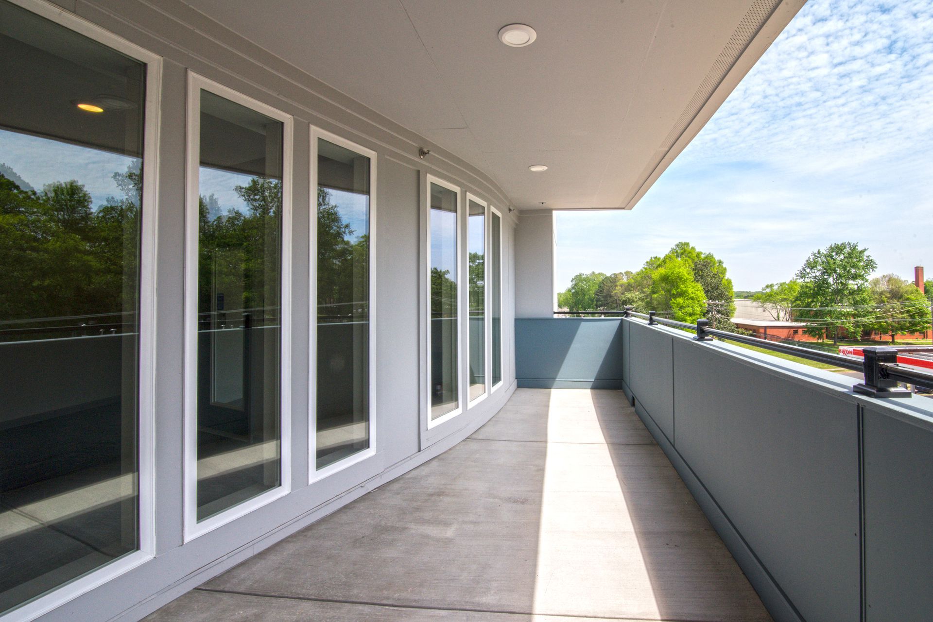 Balcony with gray floor and railing, glass doors, and blue sky at Marvel Apartments.