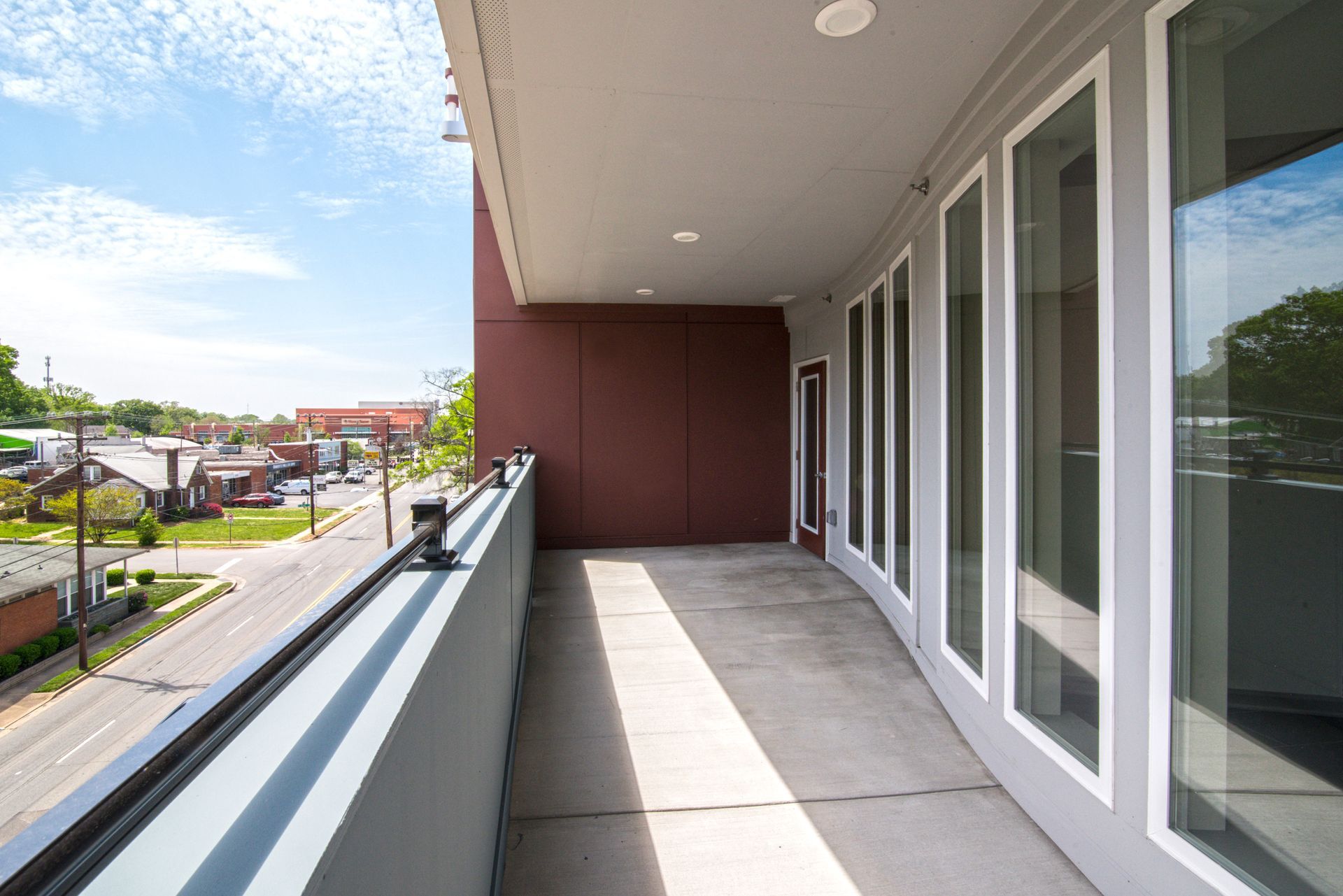 Balcony overlooking a street, with glass doors, gray walls, and blue sky at Marvel Apartments.