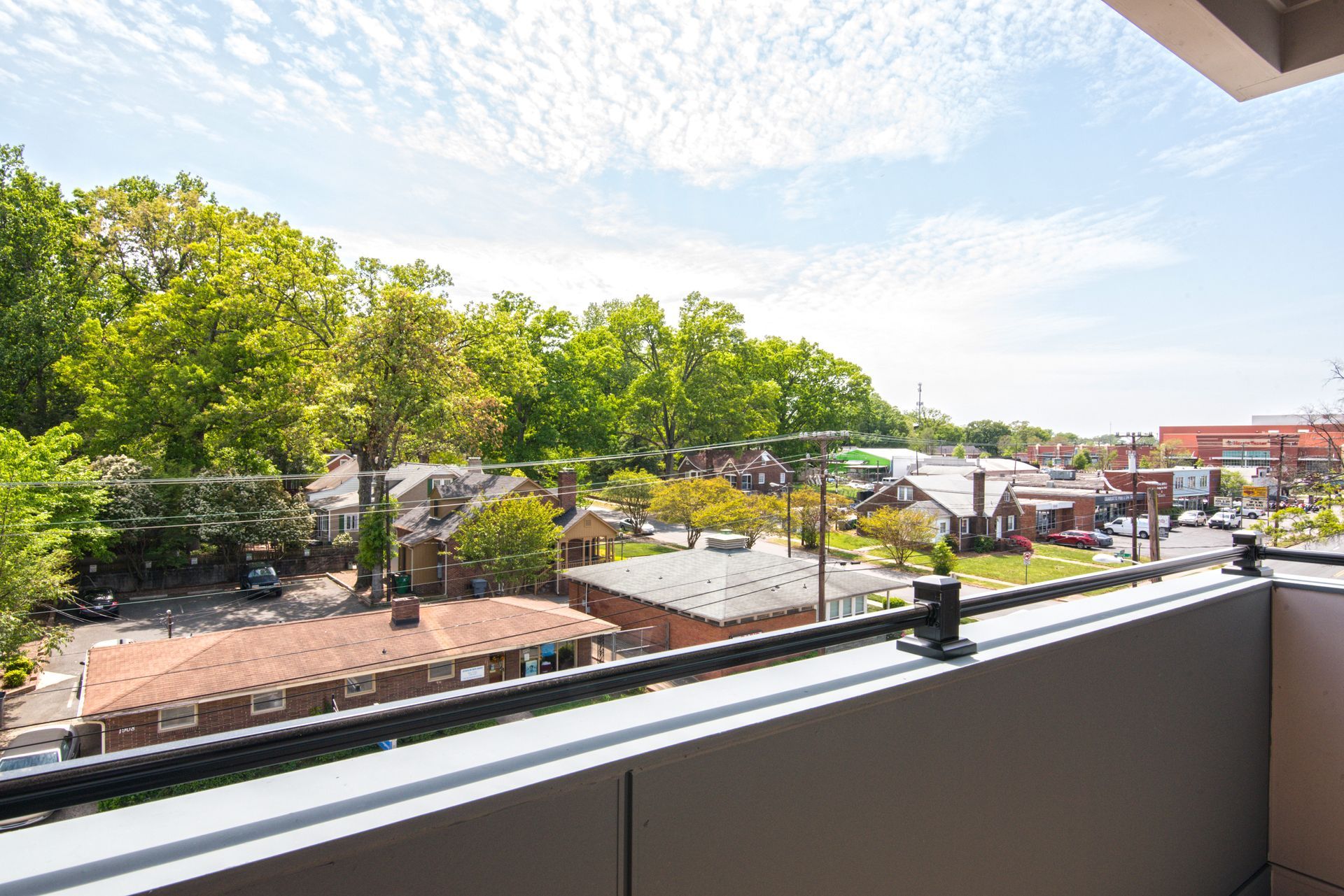 View from a balcony overlooking a neighborhood with trees and buildings under a cloudy sky.